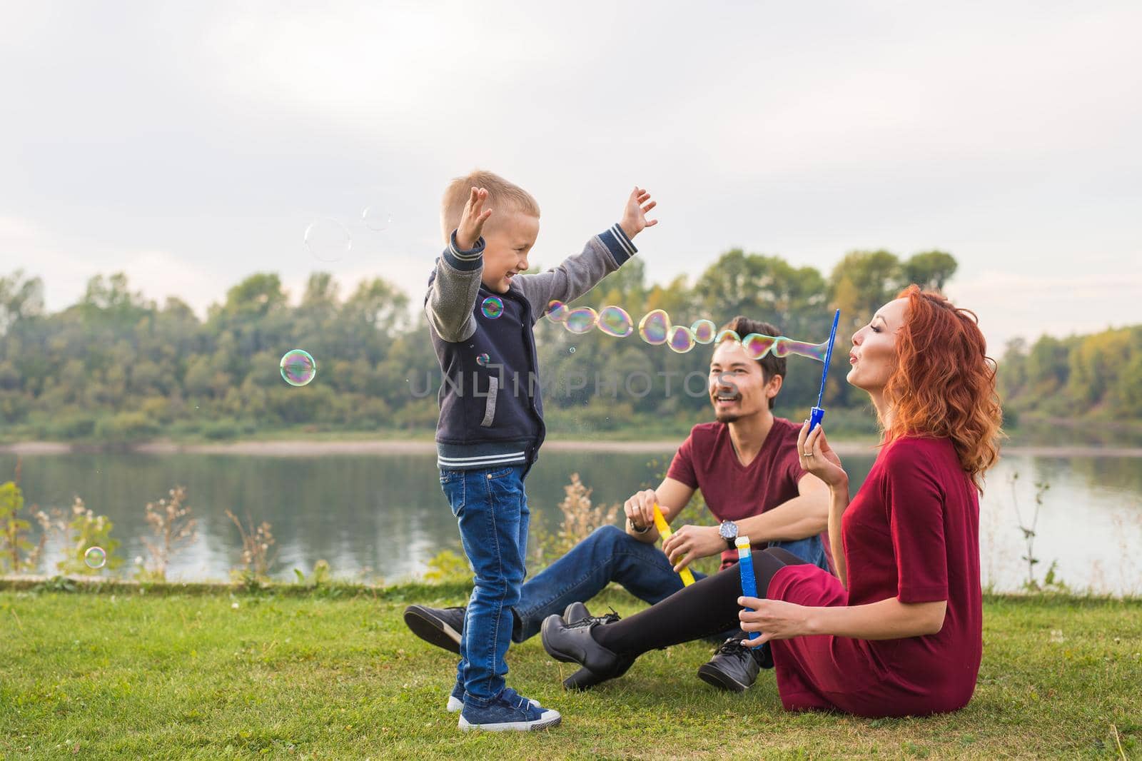 People and nature concept - Mother, father and their child playing with colorful soap bubbles.