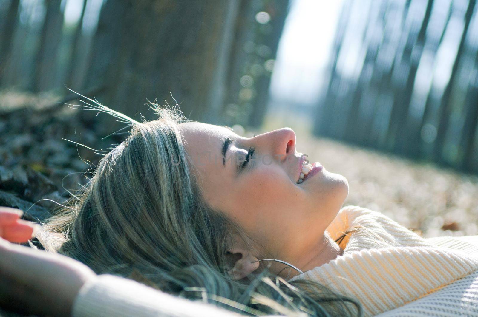 Smiling blonde girl lying on leaves in a forest of poplars by javiindy