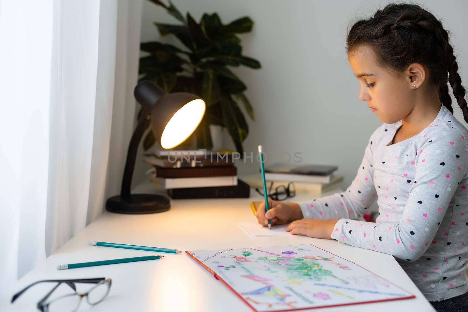 a child girl doing homework writing and reading at home by Andelov13