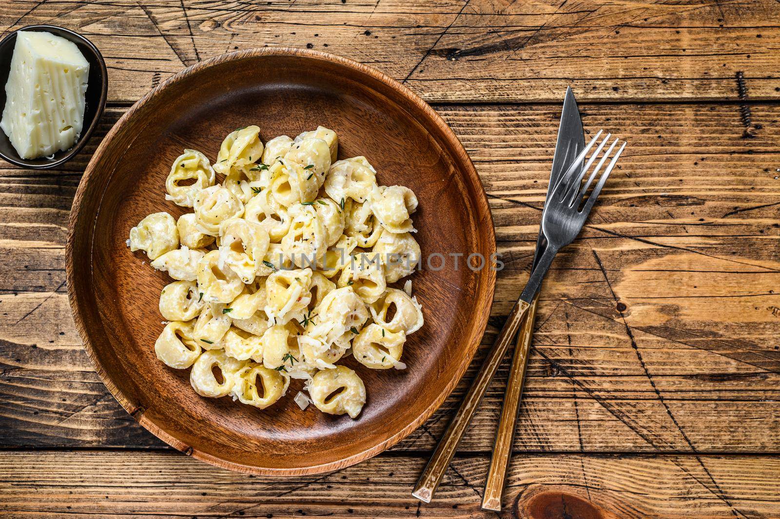 Ravioli or tortellini pasta in cream cheese sauce with meat. wooden background. Top view. Copy space.