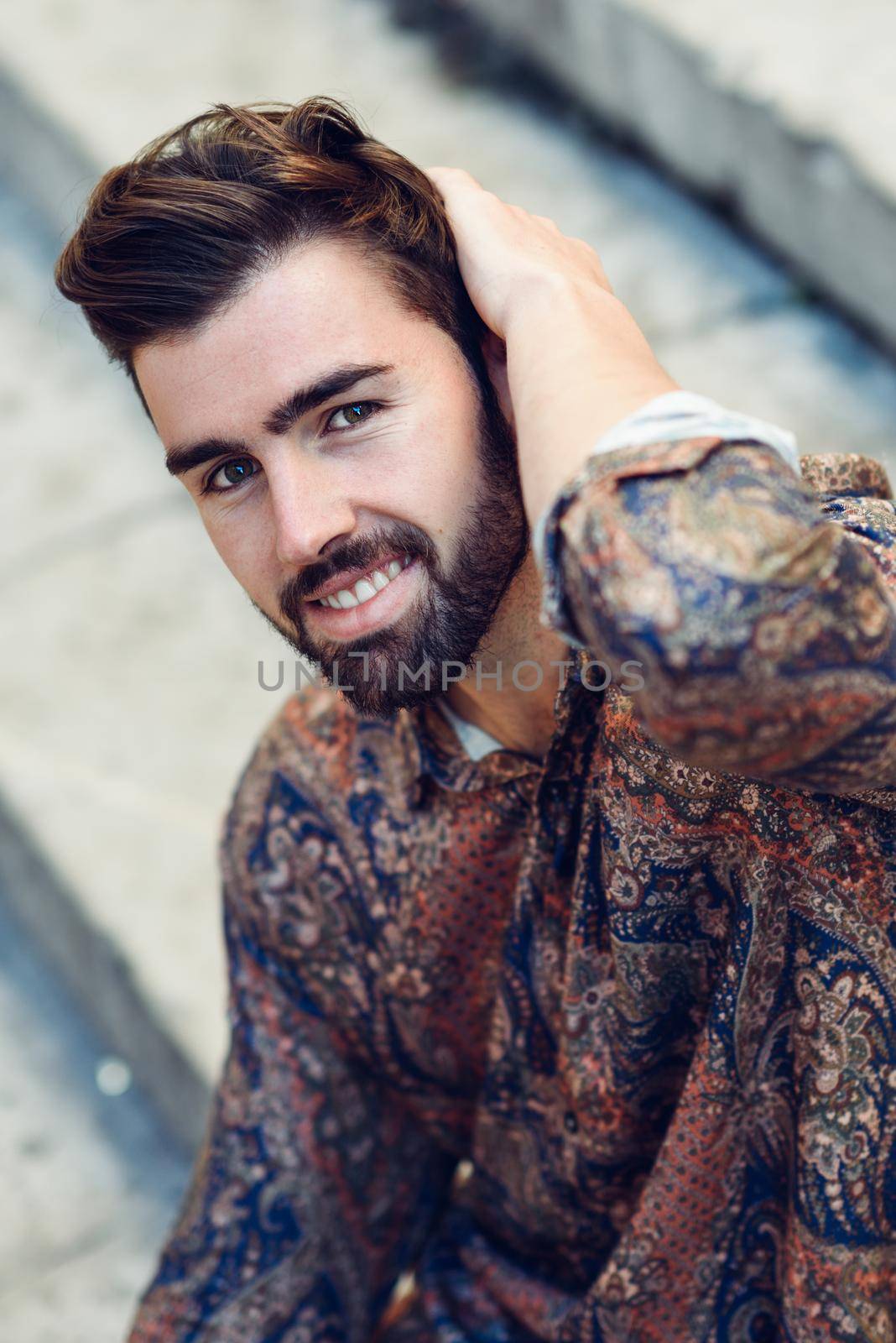 Young smiling man, model of fashion, wearing modern shirt in the street. Guy with beard and modern hairstyle in urban background.