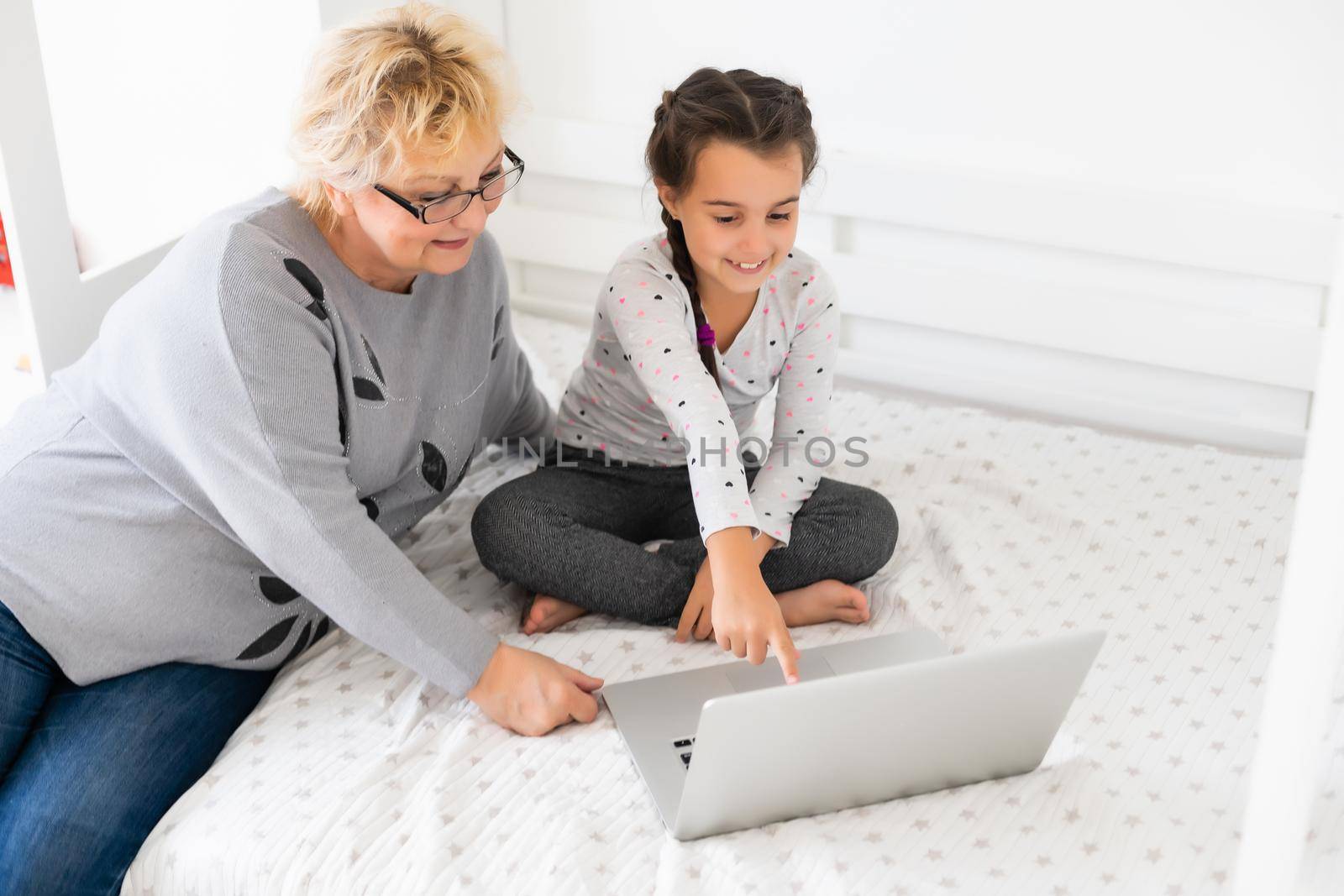 Cute and happy little girl child using laptop computer with her grandma, studying through online e-learning system. by Andelov13