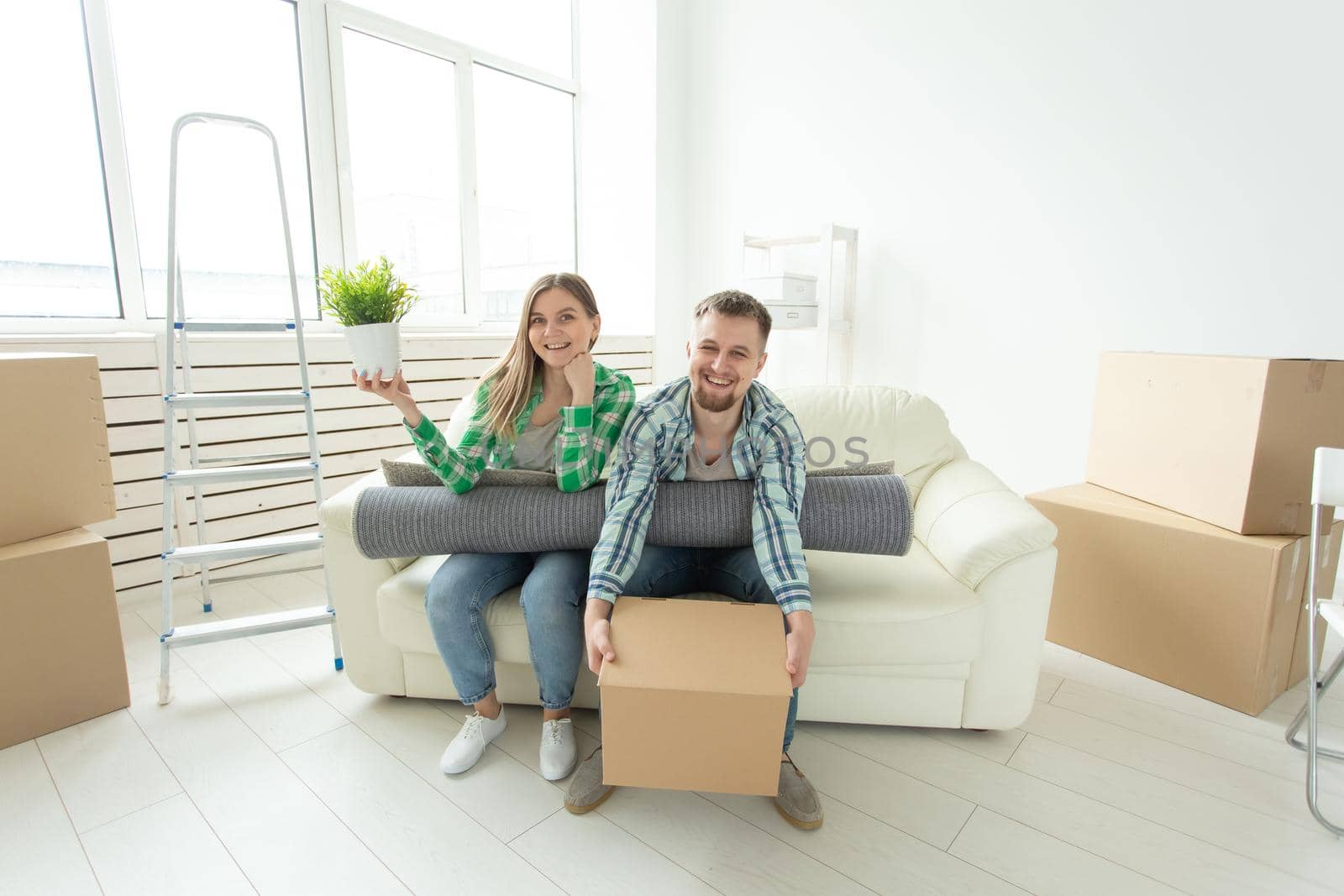 Cheerful joyful young couple charming girl and handsome man holding a box with things and a pot with a plant while moving to a new apartment. Housewarming and mortgage concept