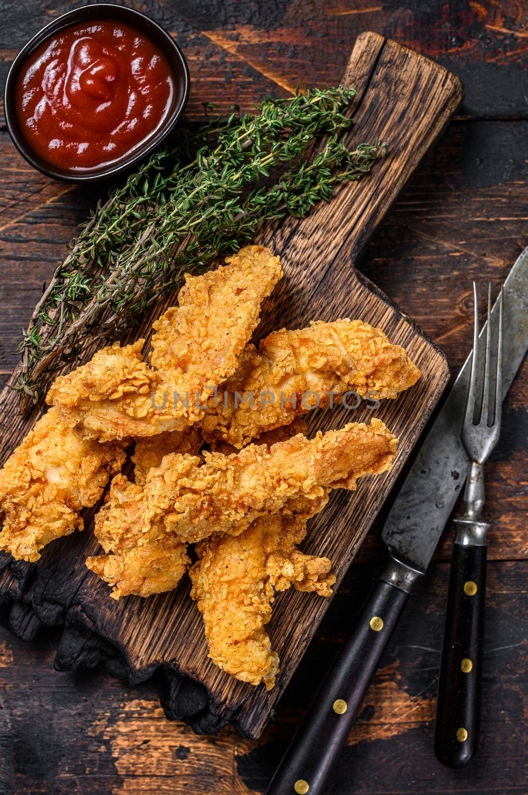 Chicken strips on a wooden cutting Board. Dark Wooden background. Top view by Composter