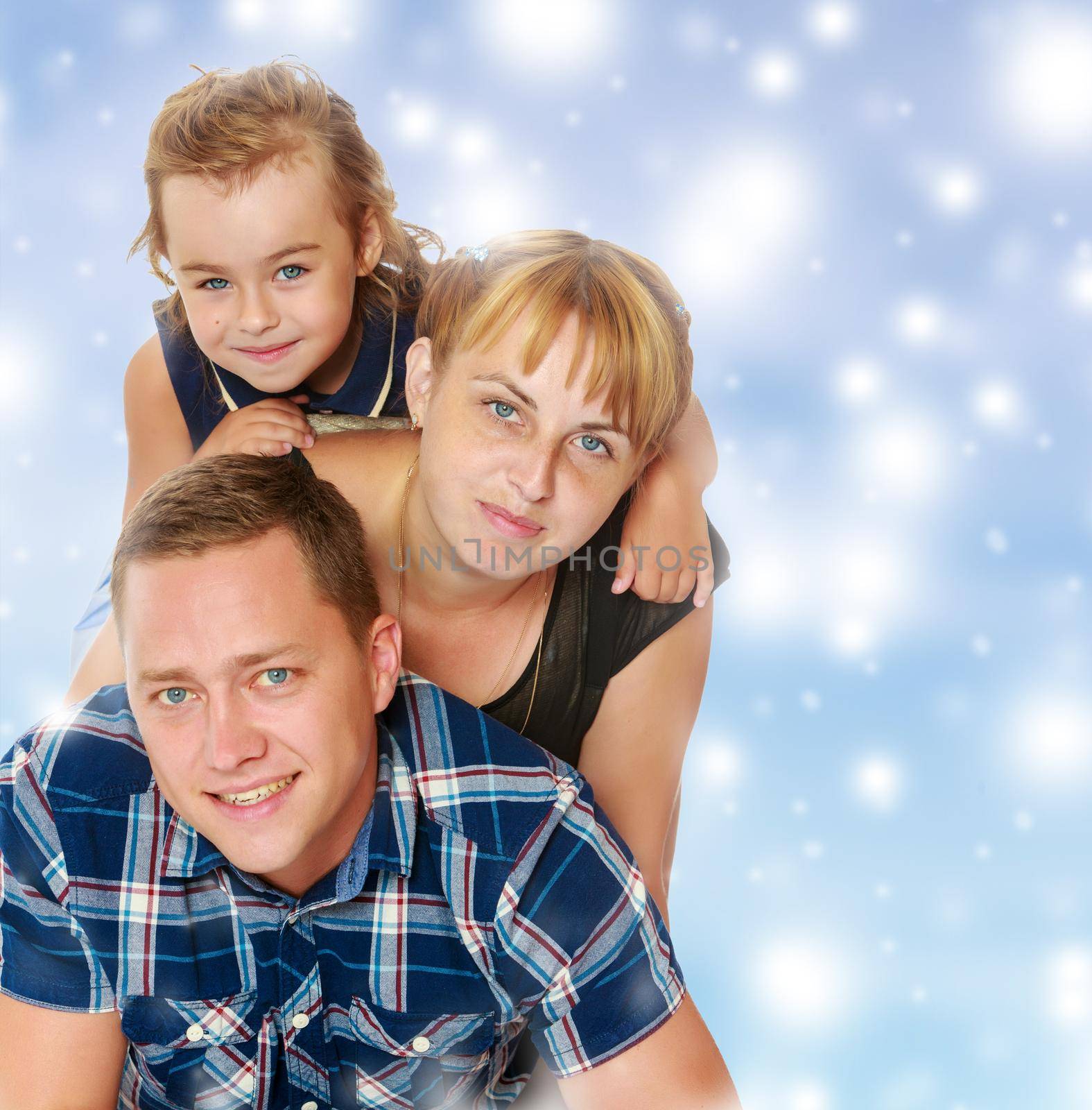 Cheerful young family of three. Mother and daughter lying on dad's back.Blue Christmas festive background with white snowflakes.