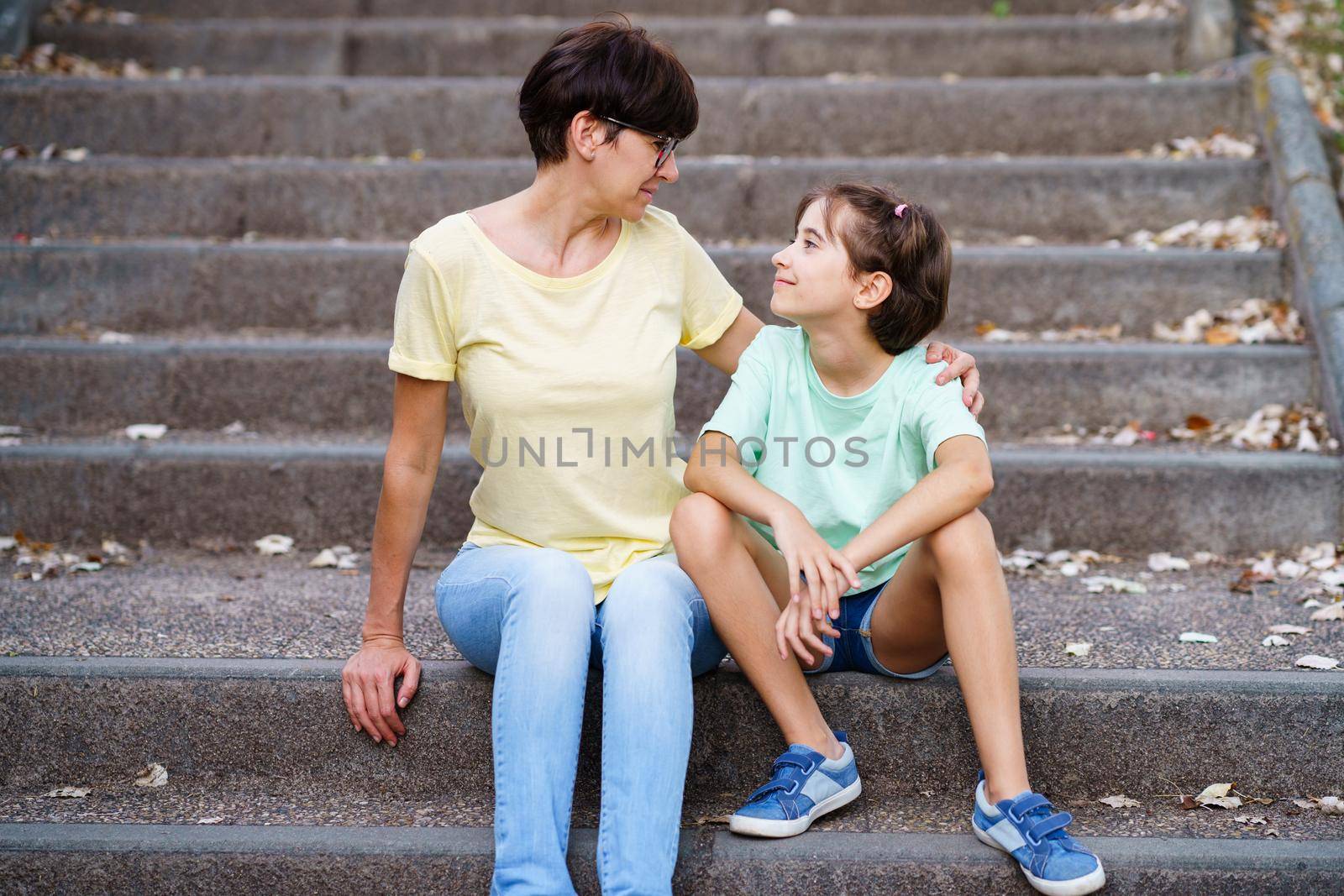 Middle-aged mother and daughter sit on the street on urban steps.