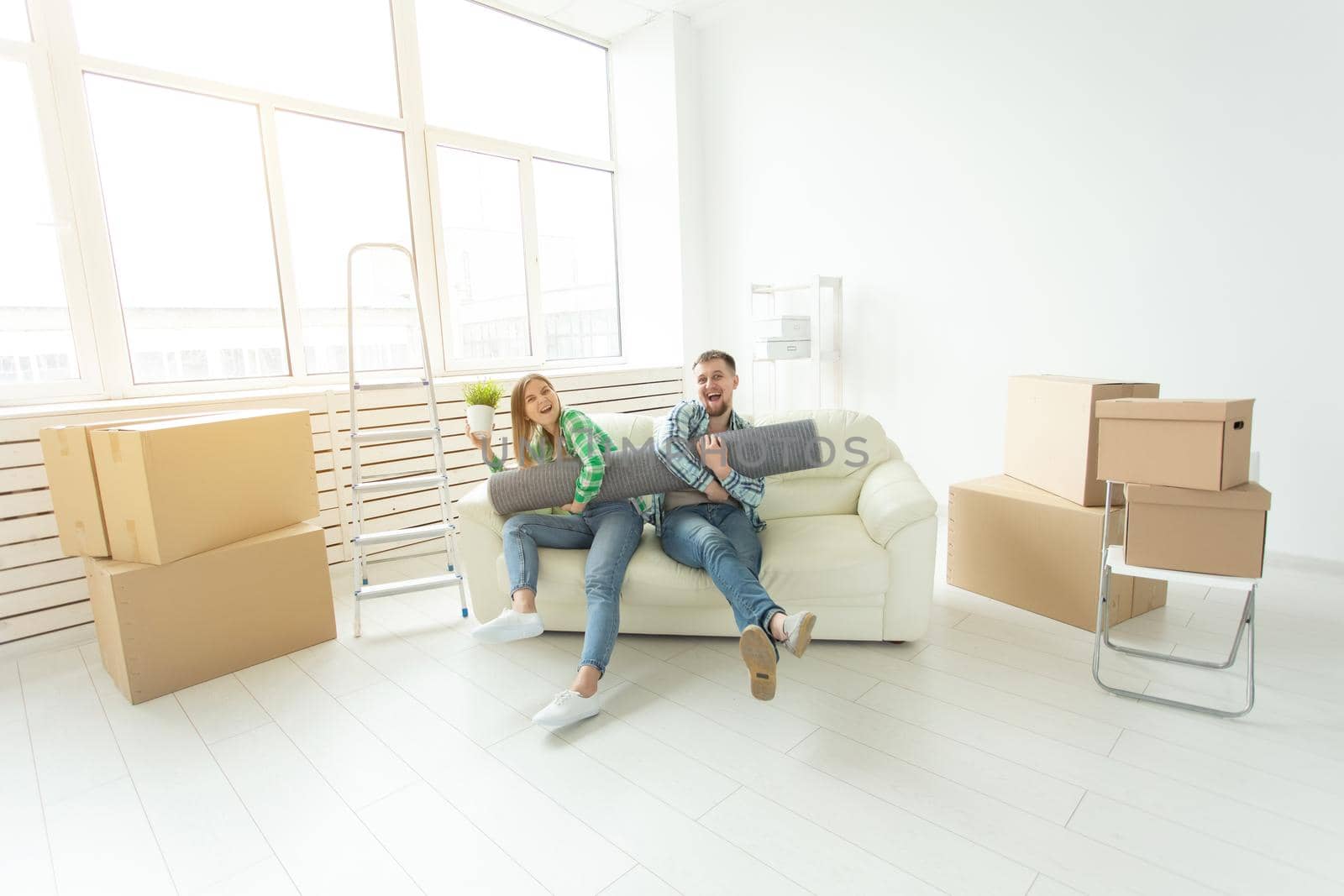 Cheerful joyful young couple charming girl and handsome man holding a box with things and a pot with a plant while moving to a new apartment. Housewarming and mortgage concept