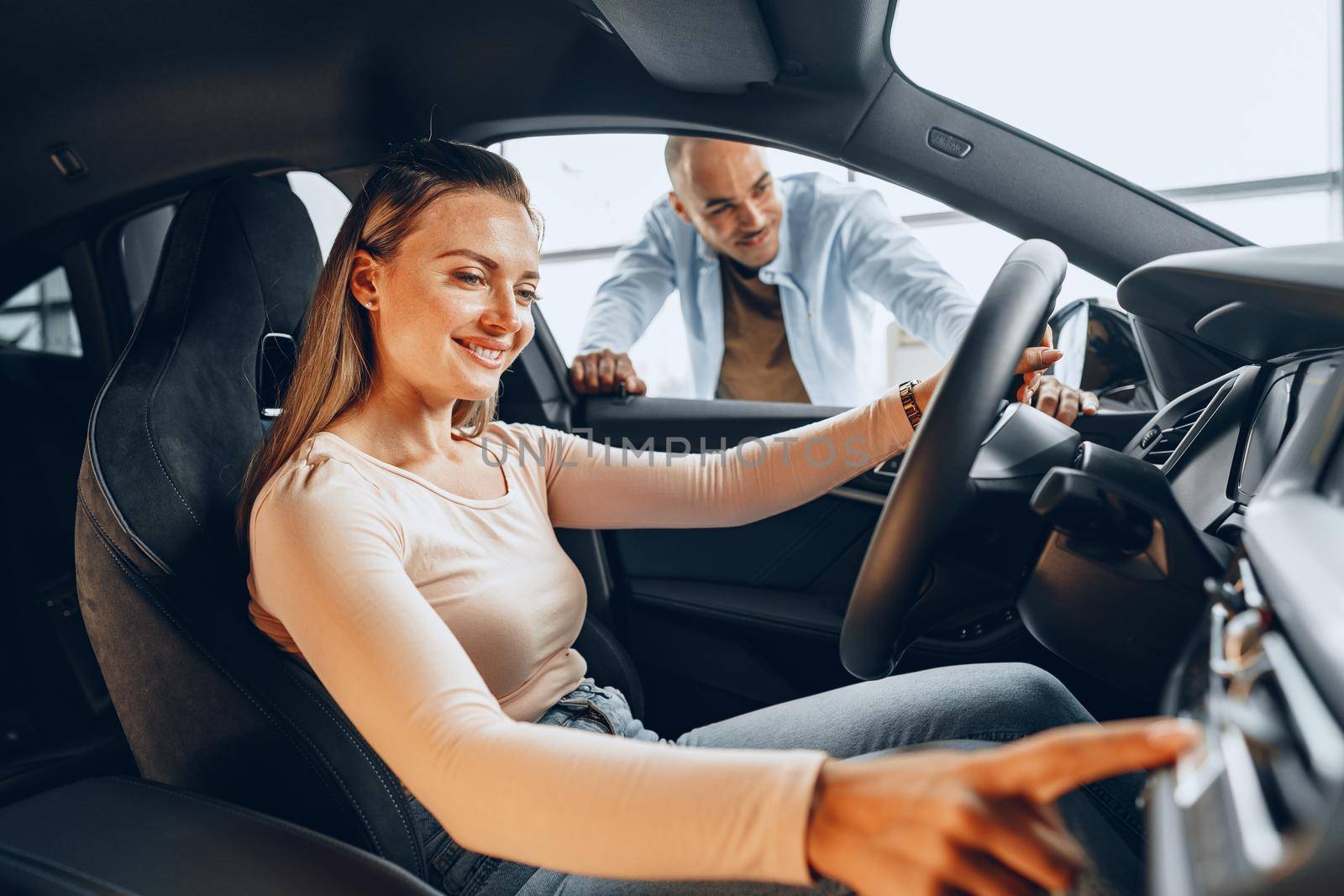 Joyful young couple looking around inside a new car they are going to buy in a car shop dealership