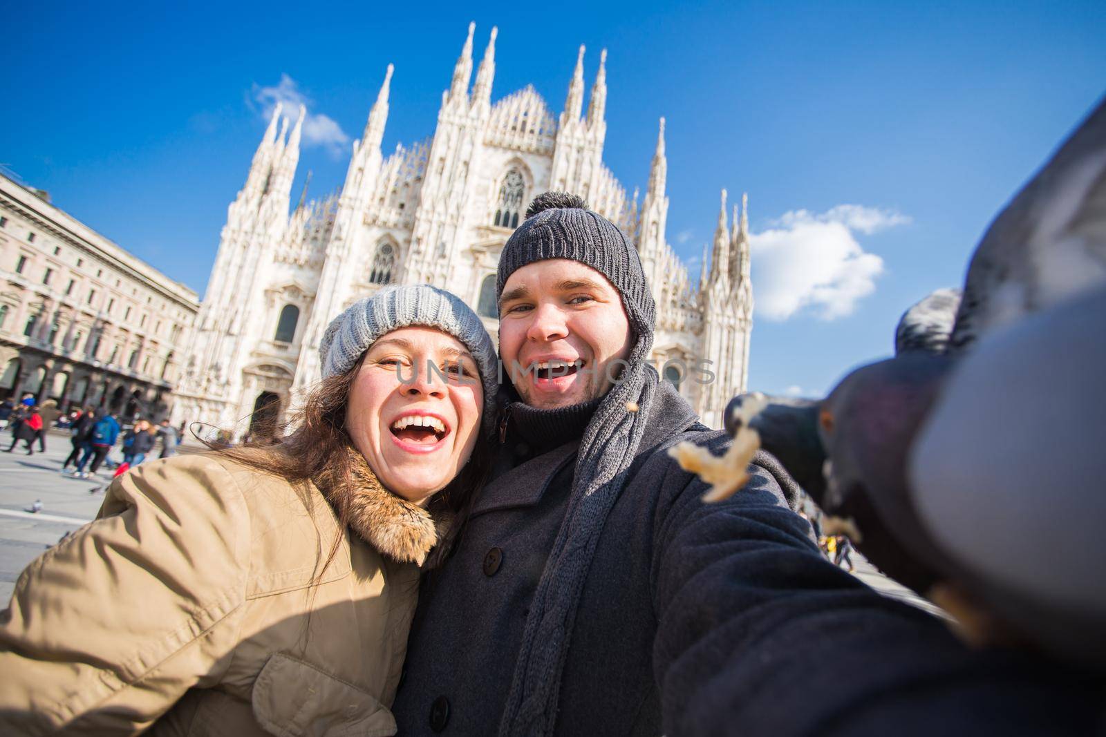Winter travel and vacations concept - Happy tourists taking a self portrait with funny pigeons in front of Duomo cathedral in Milan.