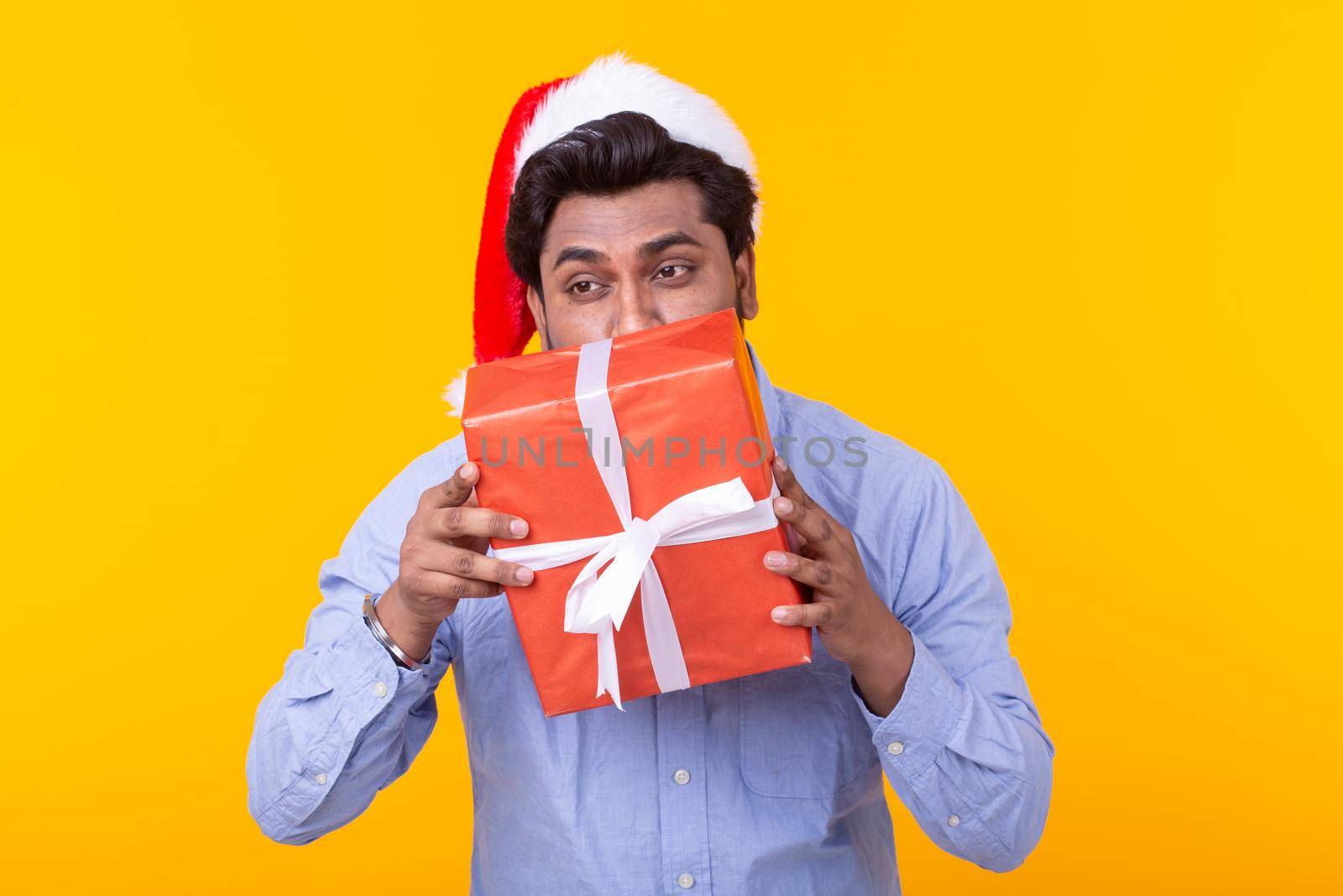 Positive young man Santa Claus with gifts and Christmas tree posing on a yellow background. Christmas and New Year holidays concept. Advertising space