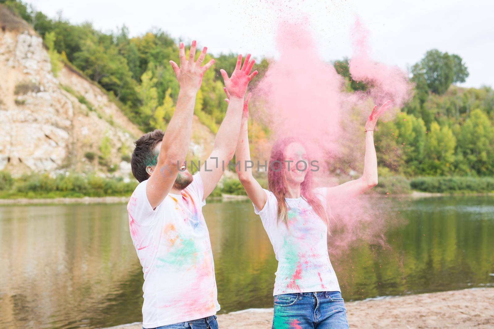 Festival holi, holidays, tourism and nature concept - Couple dressed in white shirts playing with colorful dust.