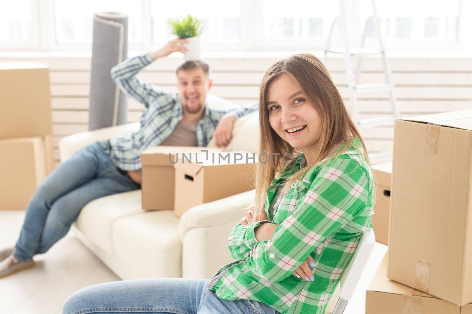 Positive smiling young girl sitting against her laughing blurred husband in a new living room while moving to a new home. The concept of joy from the possibility of finding new housing. by Satura86