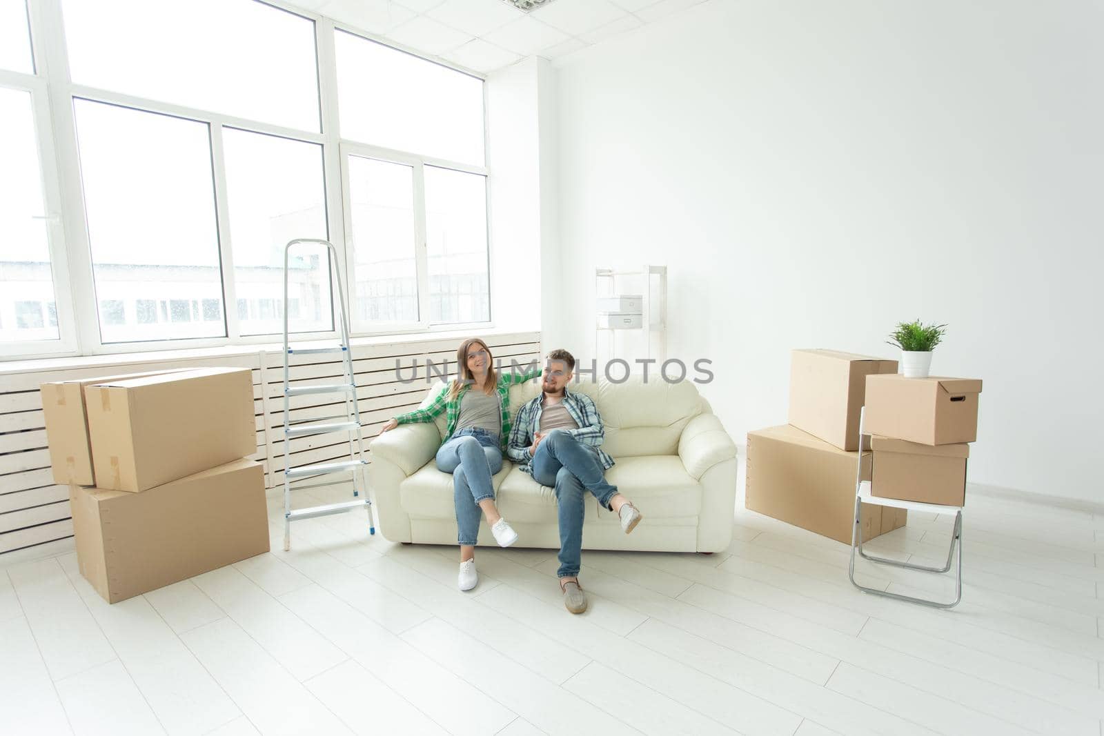 Cheerful joyful young couple charming girl and handsome man holding a box with things and a pot with a plant while moving to a new apartment. Housewarming and mortgage concept