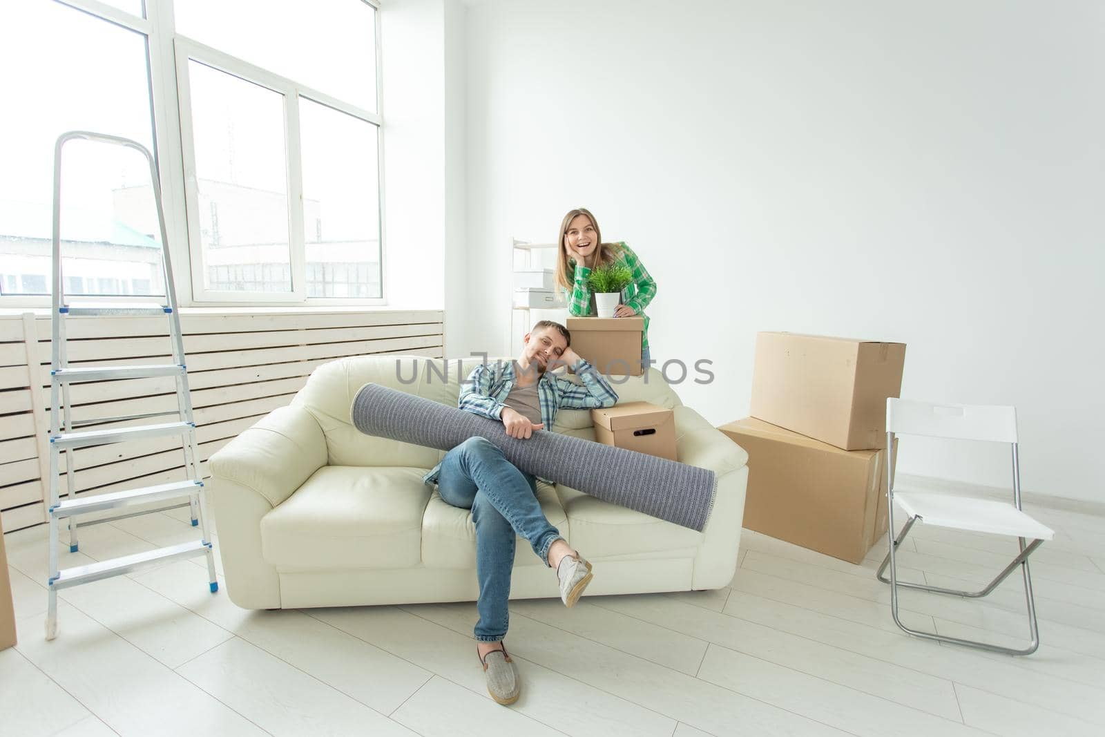 Satisfied cheerful young couple strong man and pretty woman holding their things in their hands sitting in the living room of a new apartment. Housewarming concept. by Satura86