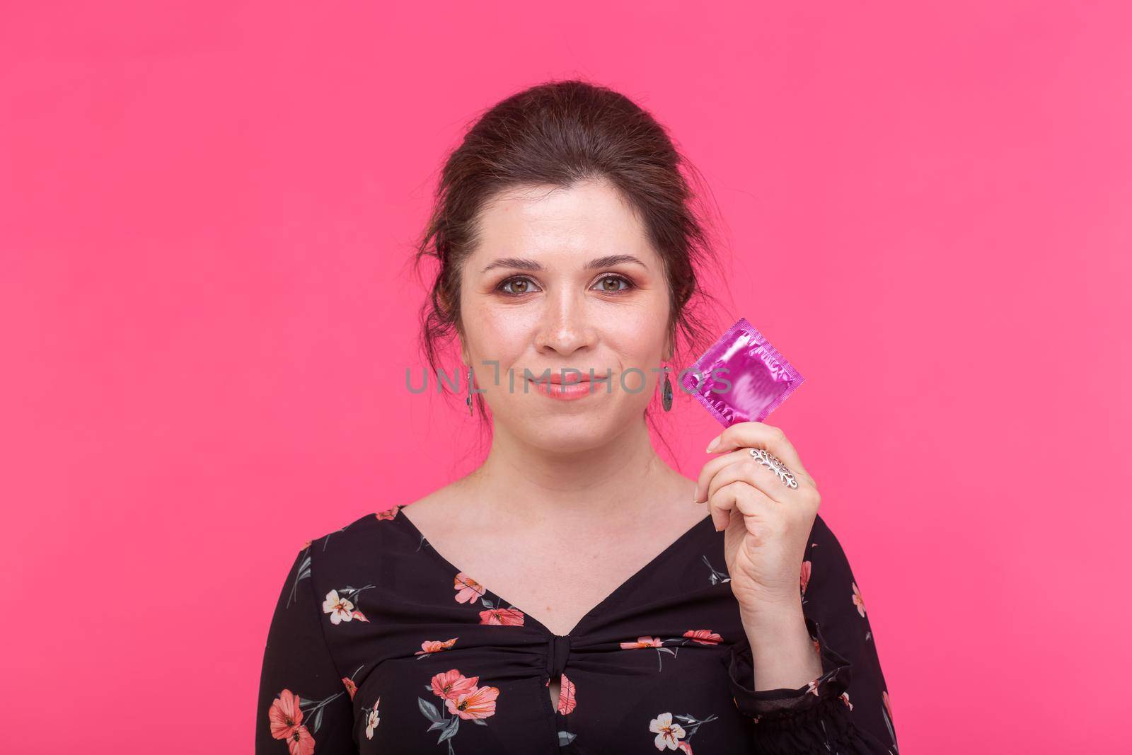 Safe sex, health and contraception concept - woman holding in hands a condom on pink background.
