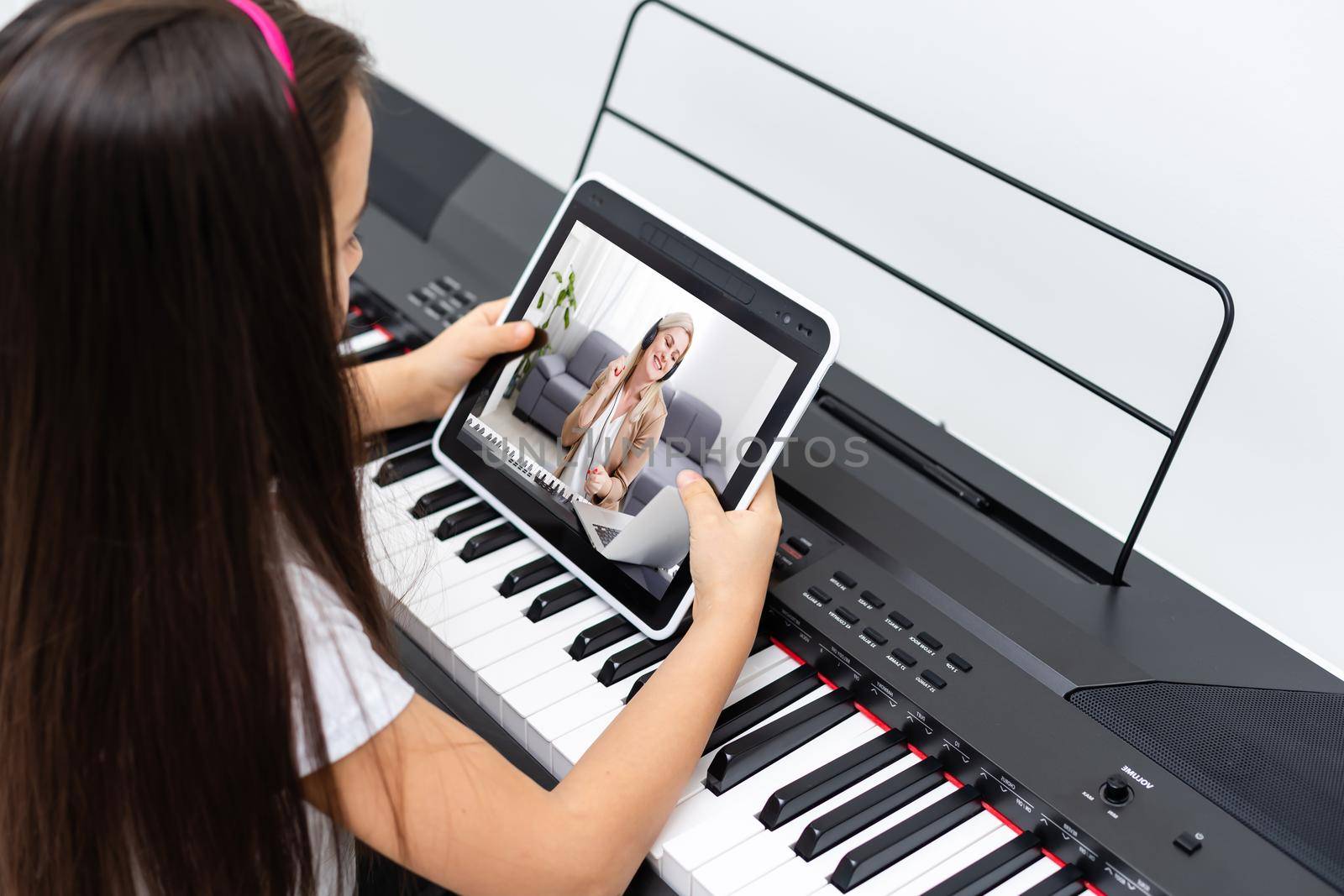 A little girl learns to play the piano from video lessons. Online distance learning during covid-19 by Andelov13
