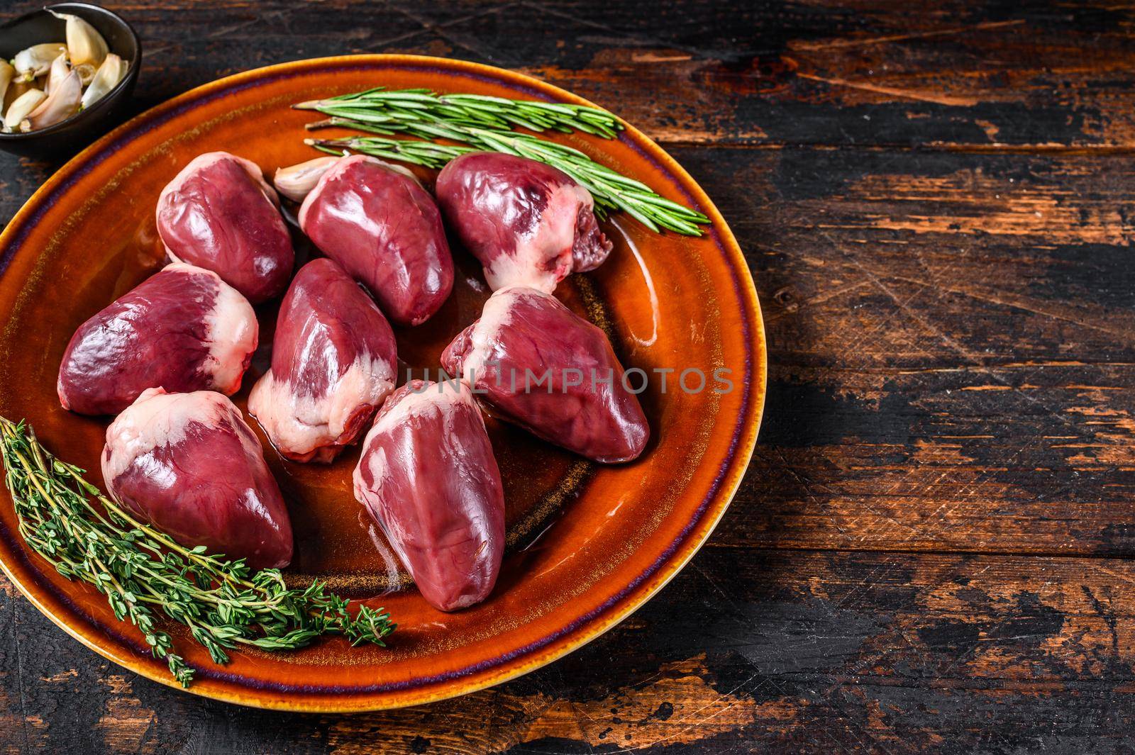 Fresh Raw turkey hearts offal giblets with thyme and rosemary. Dark wooden background. Top view. Copy space.