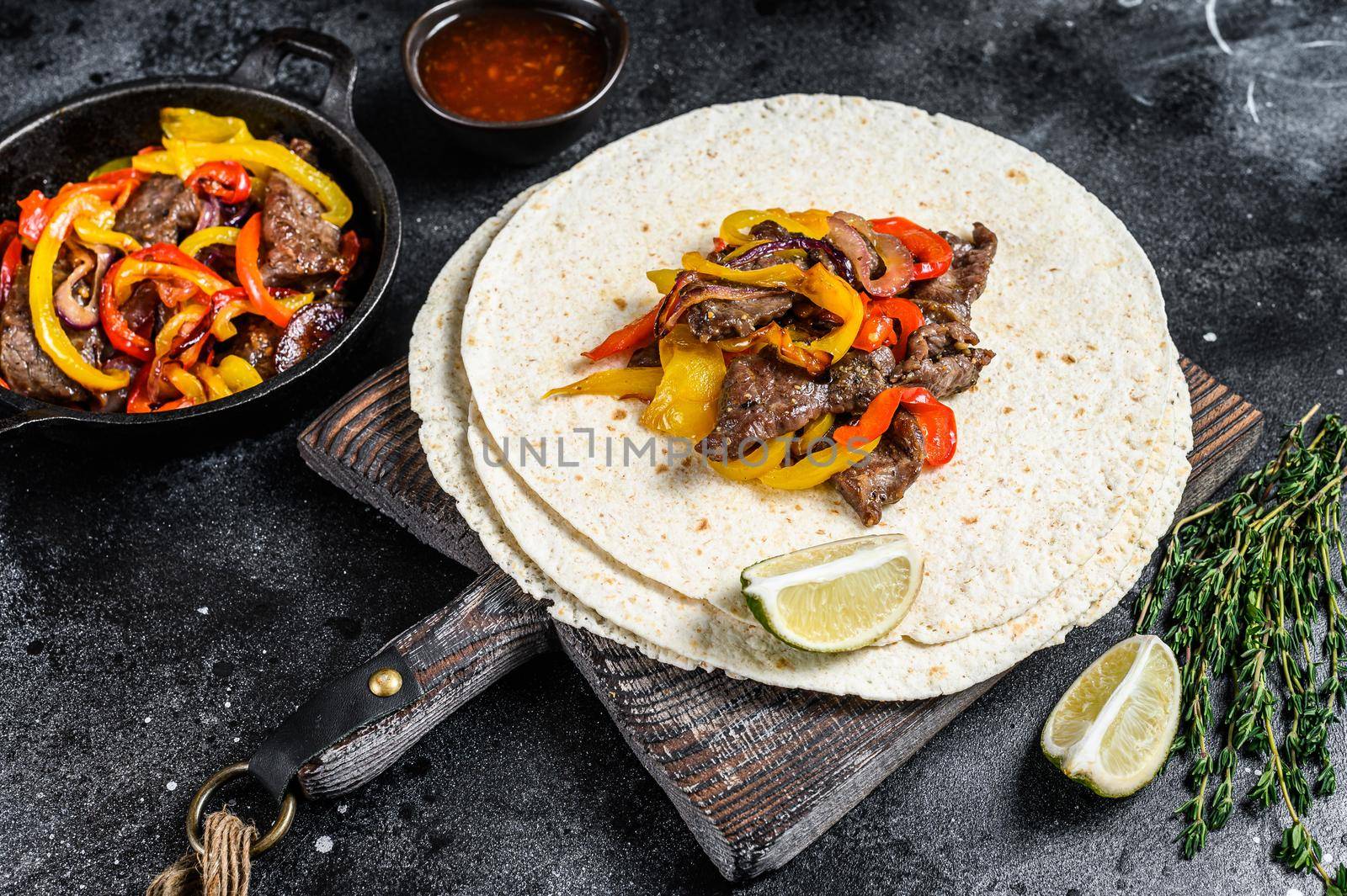 Mexican Fajitas with colored pepper and onions, served with tortillas and salsa. Black background. Top view by Composter
