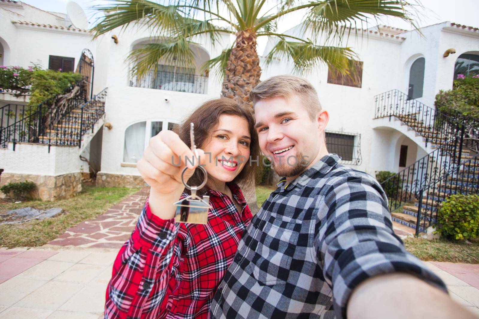 Moving and real estate concept - Happy young laughing cheerful couple man and woman holding their new home keys in front of a house