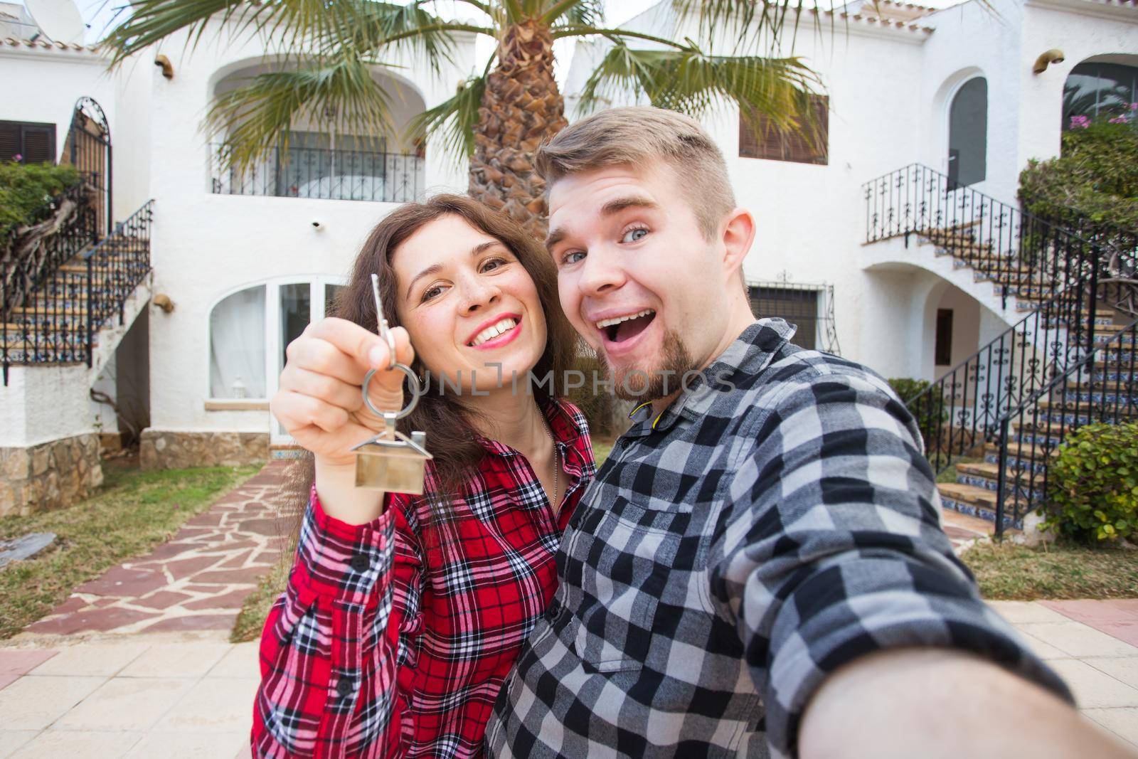 Moving and real estate concept - Happy young laughing cheerful couple man and woman holding their new home keys in front of a house