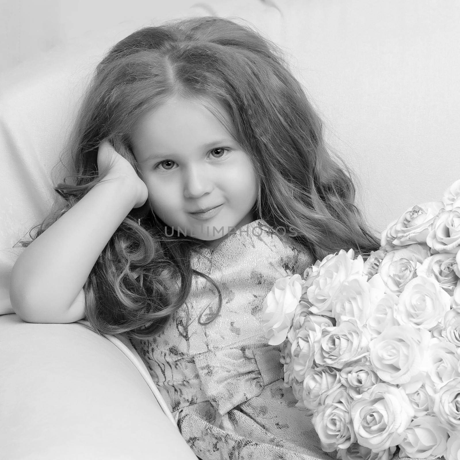 Happy little girl with a bouquet of flowers sitting on the couch. The concept of a holiday, a spring mood.