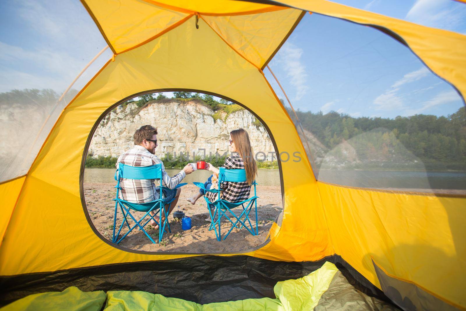 people, summer tourism and nature concept - young couple resting near camping tent.