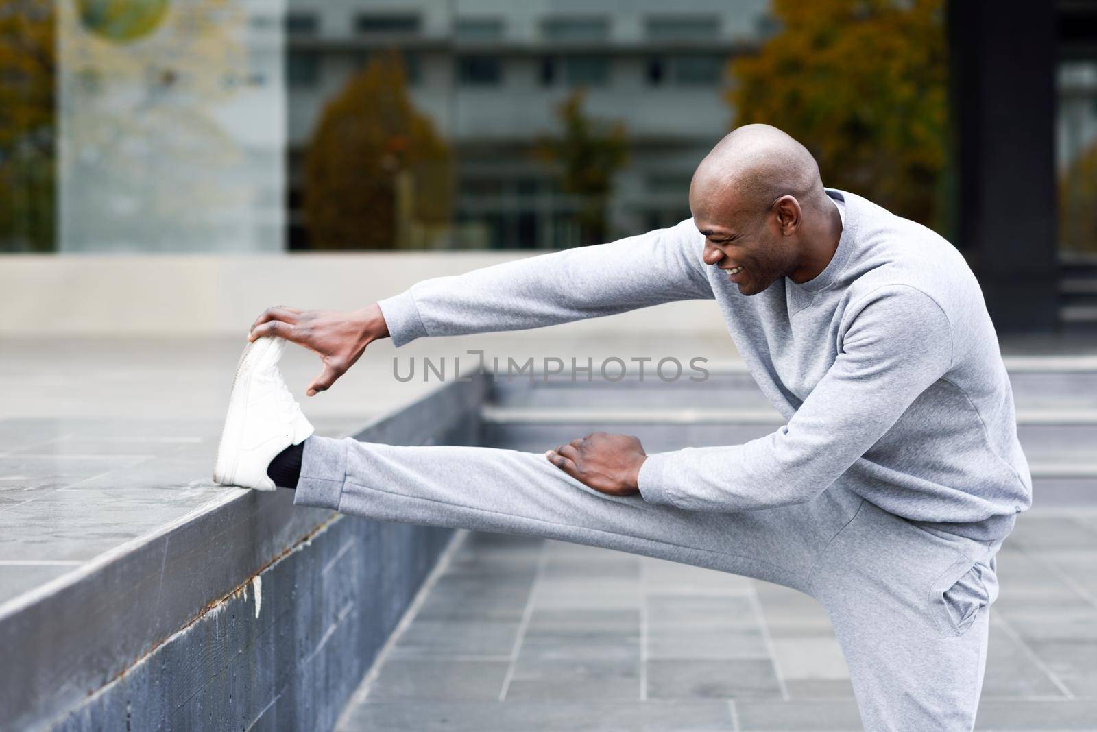 Black man doing stretching before running in urban background. Young male exercising