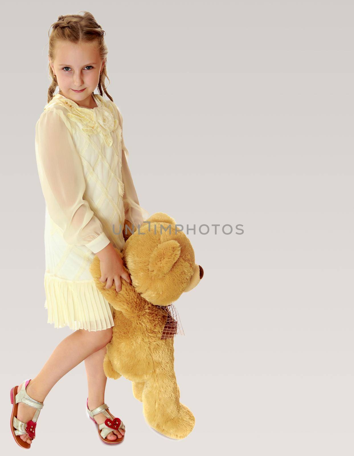 Beautiful little girl in stylish white dress, holding a Teddy bear. Full growth.On a gray background.