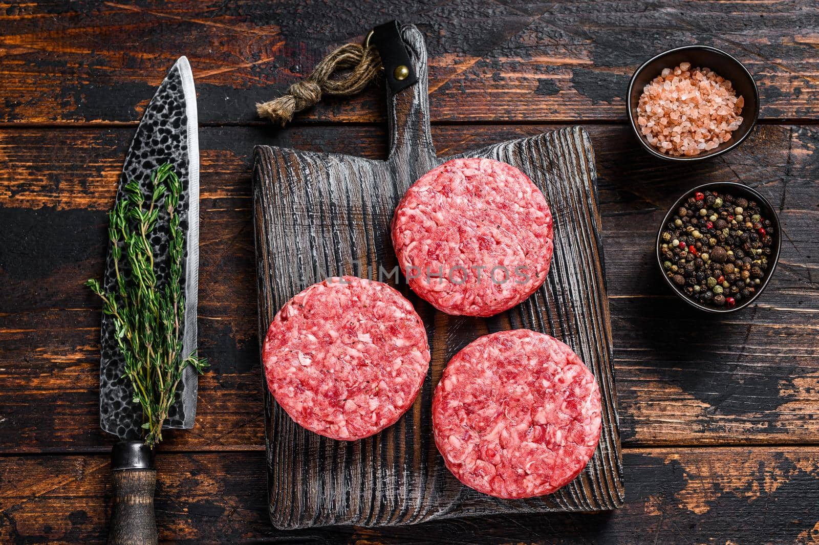 Raw steak burgers patties with ground beef and thyme on a wooden cutting board. Dark Wooden background. Top view.