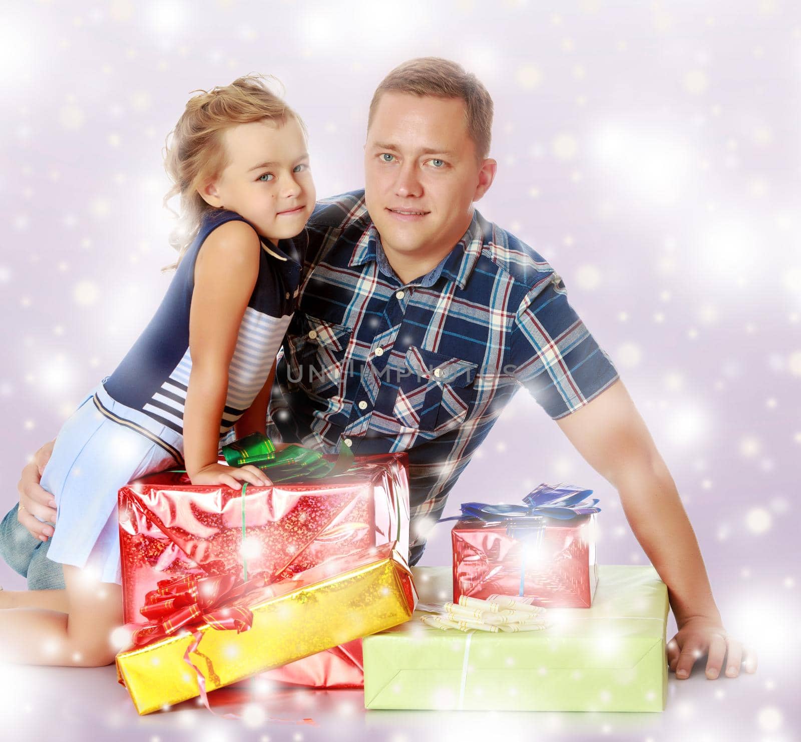Cute little girl with her favorite dad, sitting on the floor surrounded by a variety of beautifully packaged boxes with gifts.Blue Christmas festive background with white snowflakes.