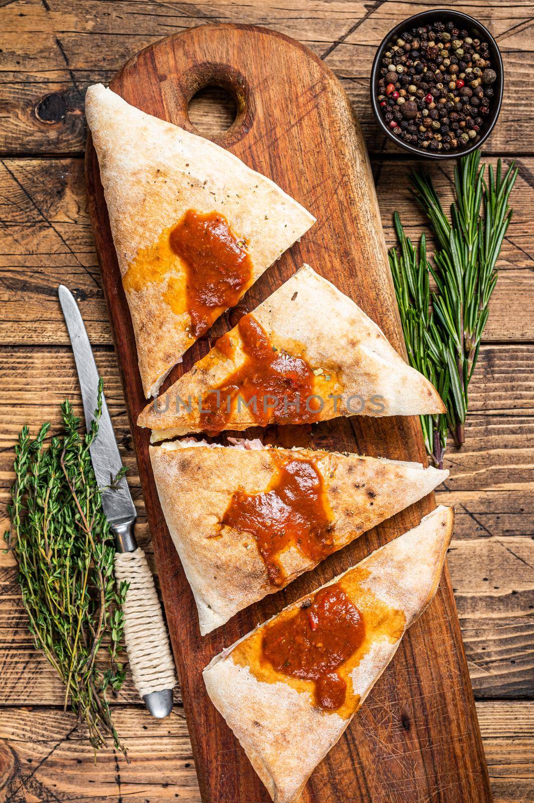 Cut and sliced Calzone closed pizza with ham and cheese on wooden board with hot tomato sauce. wooden background. Top view.
