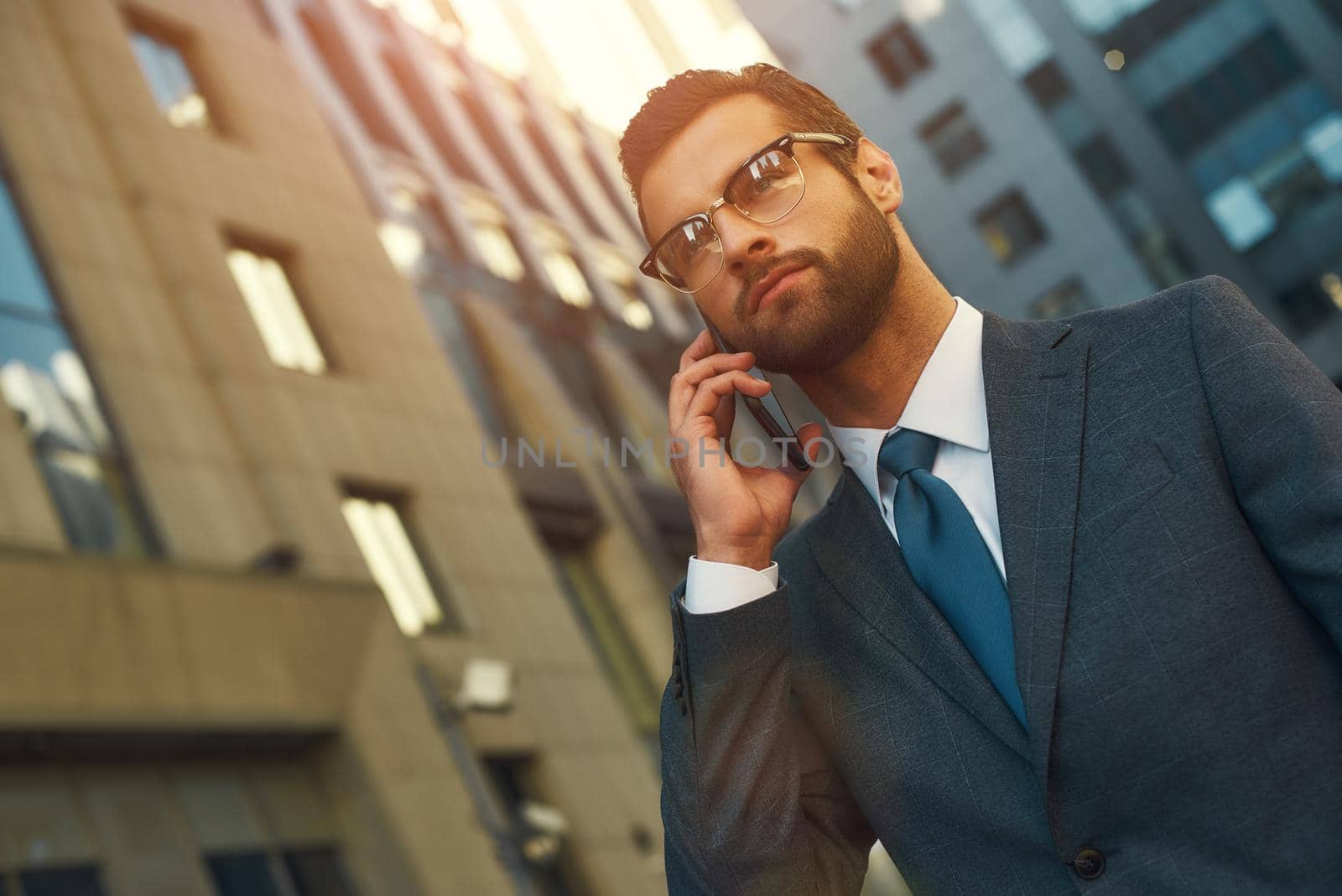 Busy day. Portrait of handsome bearded man in suit talking by phone with client while walking outdoors by friendsstock