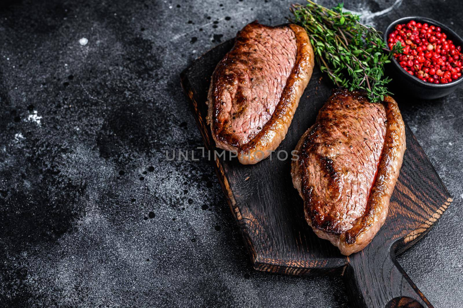 BBQ Grilled top sirloin cap or picanha steak on a wooden cutting board. Black background. Top view. Copy space.