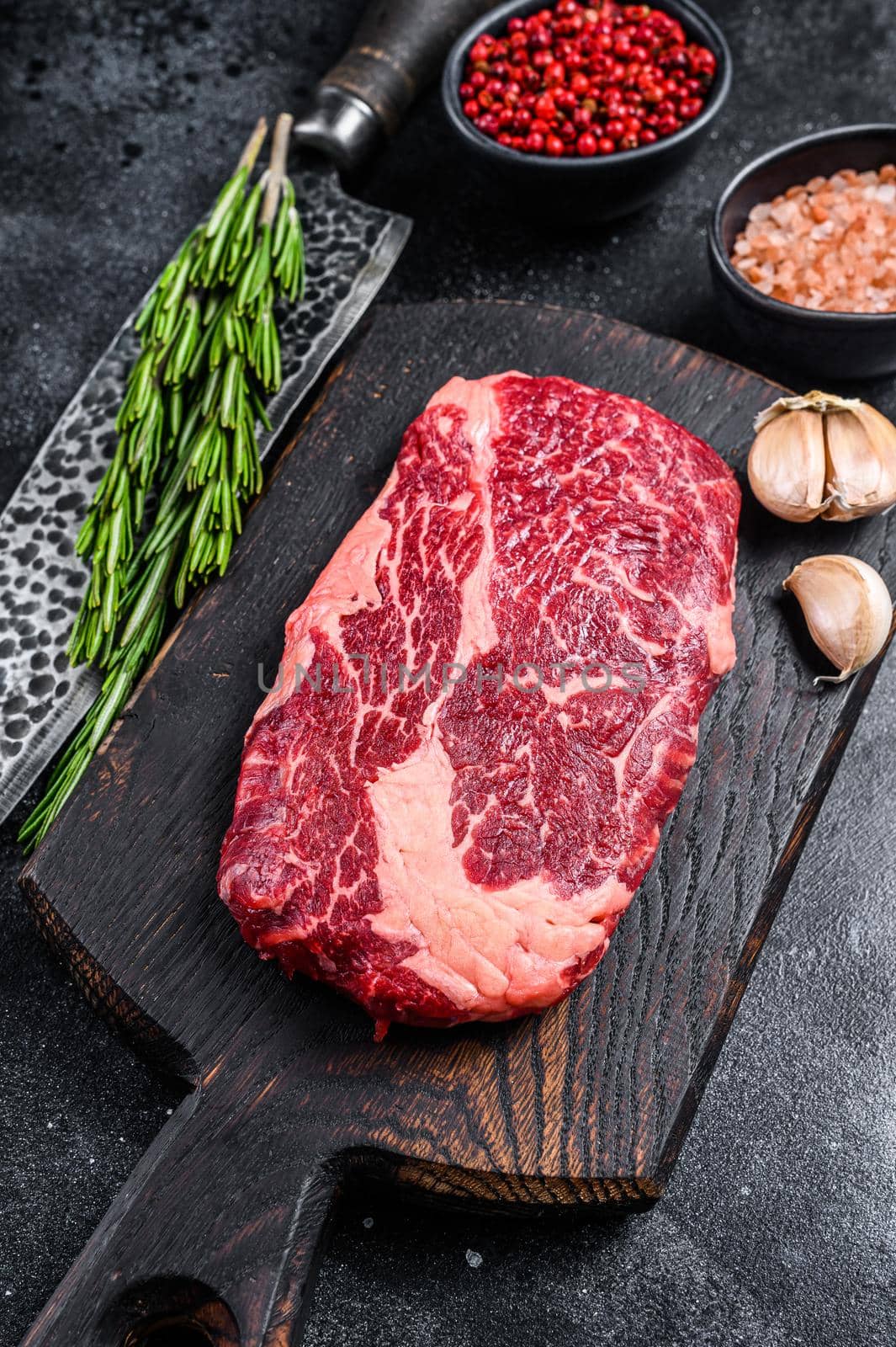 Black angus ribeye, raw rib-eye beef steak on a wooden board with knife. Black background. Top view.