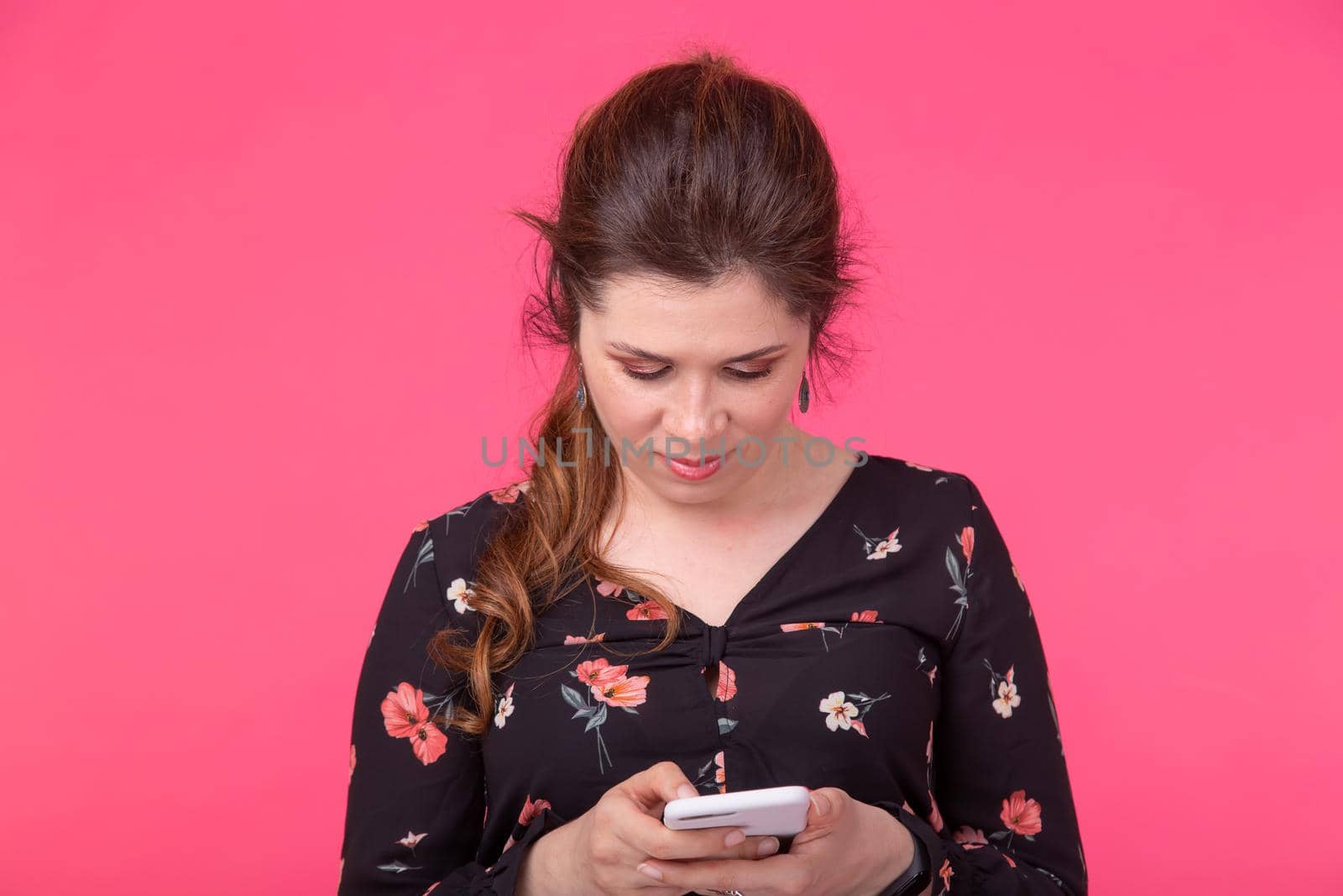 Communication and technologies concept - Portrait of a woman sending text message from her phone on pink background.