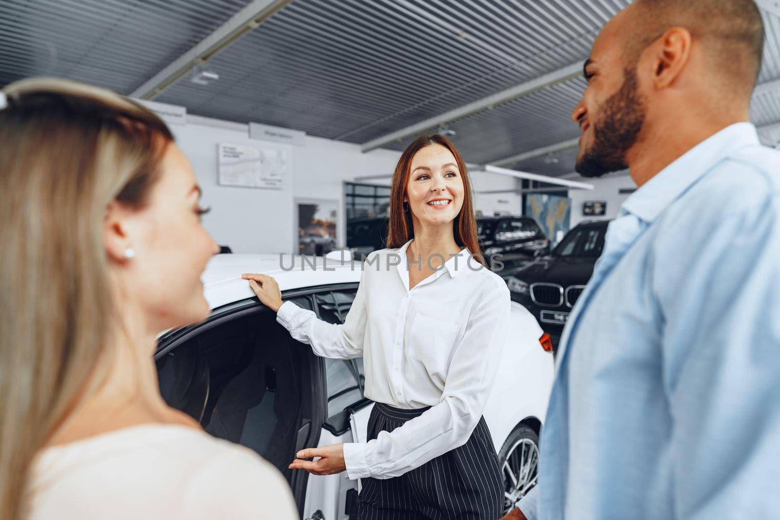 Woman car dealer explaining to buyers features of their new car by Fabrikasimf