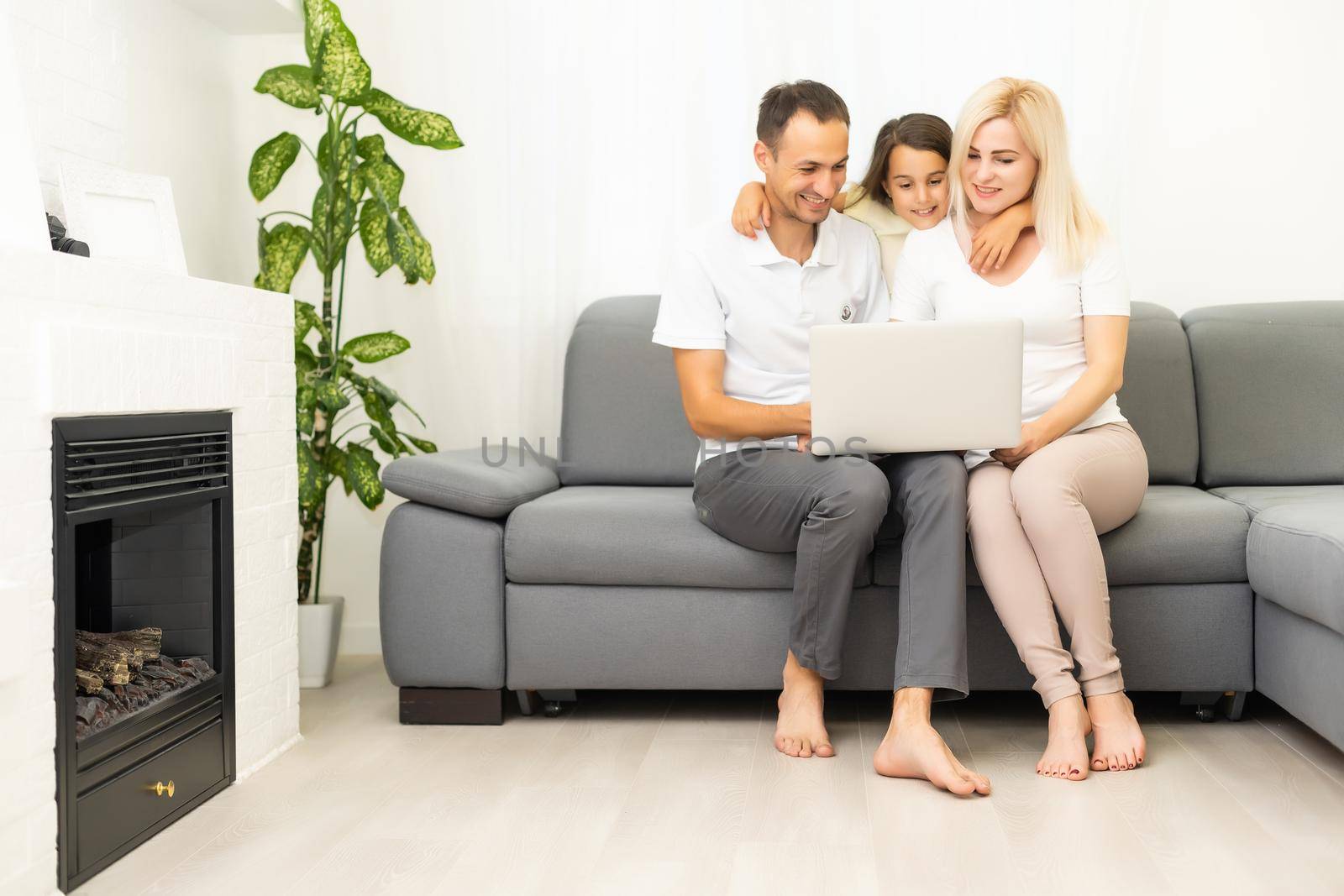 Happy family with kid girl having fun using laptop together sitting on sofa, parents and child daughter laughing relaxing at home with computer watching funny internet video, making online call by Andelov13