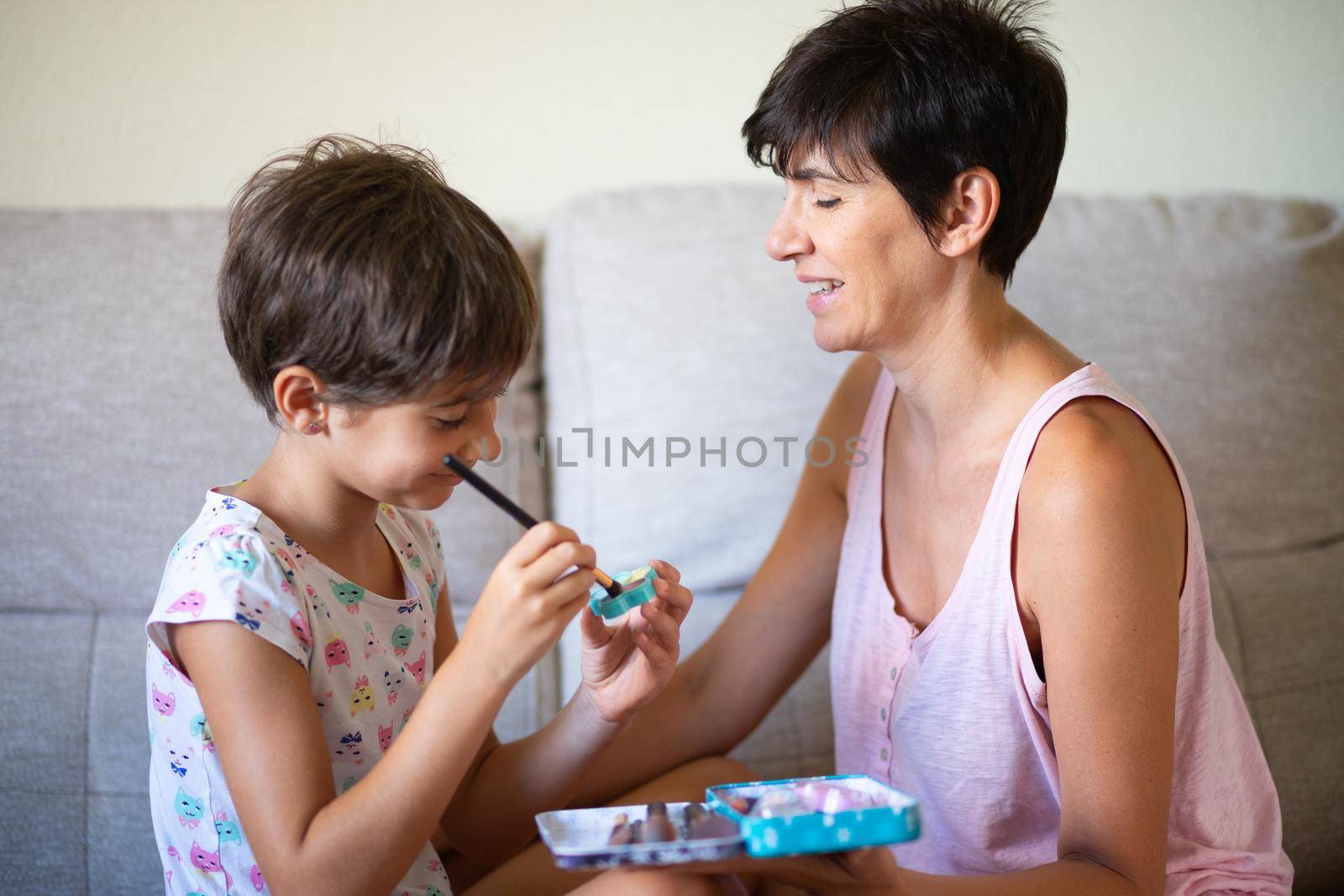 Happy beautiful mother and her little cute daughter doing make up for each other. Mum spending free time with her daughter.