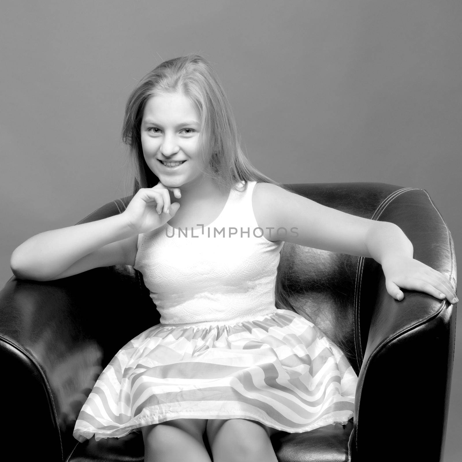 Beautiful teen girl sits in the studio on a leather chair. Concept of youth fashion and culture.