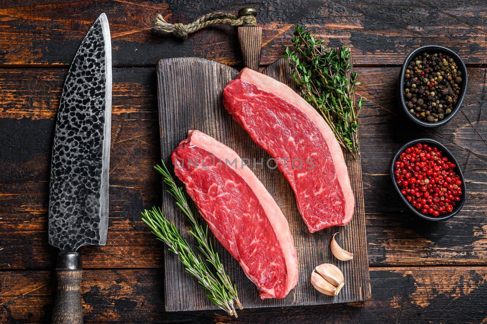 Raw top sirloin beef meat steak on a cutting wooden board. Dark wooden background. Top view by Composter