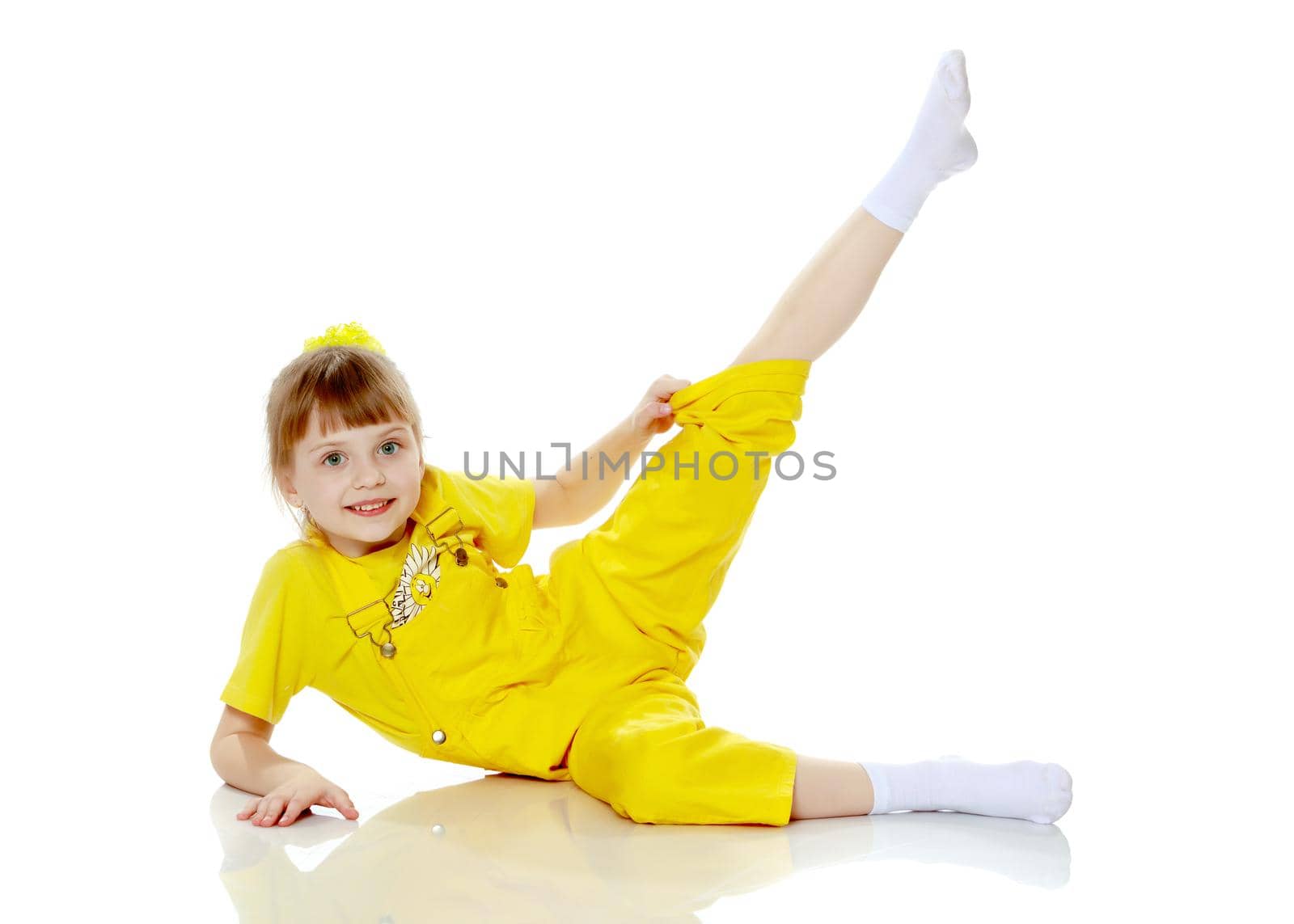 Girl with a short bangs on her head and bright yellow overalls.She crouched down on the white advertising banner.