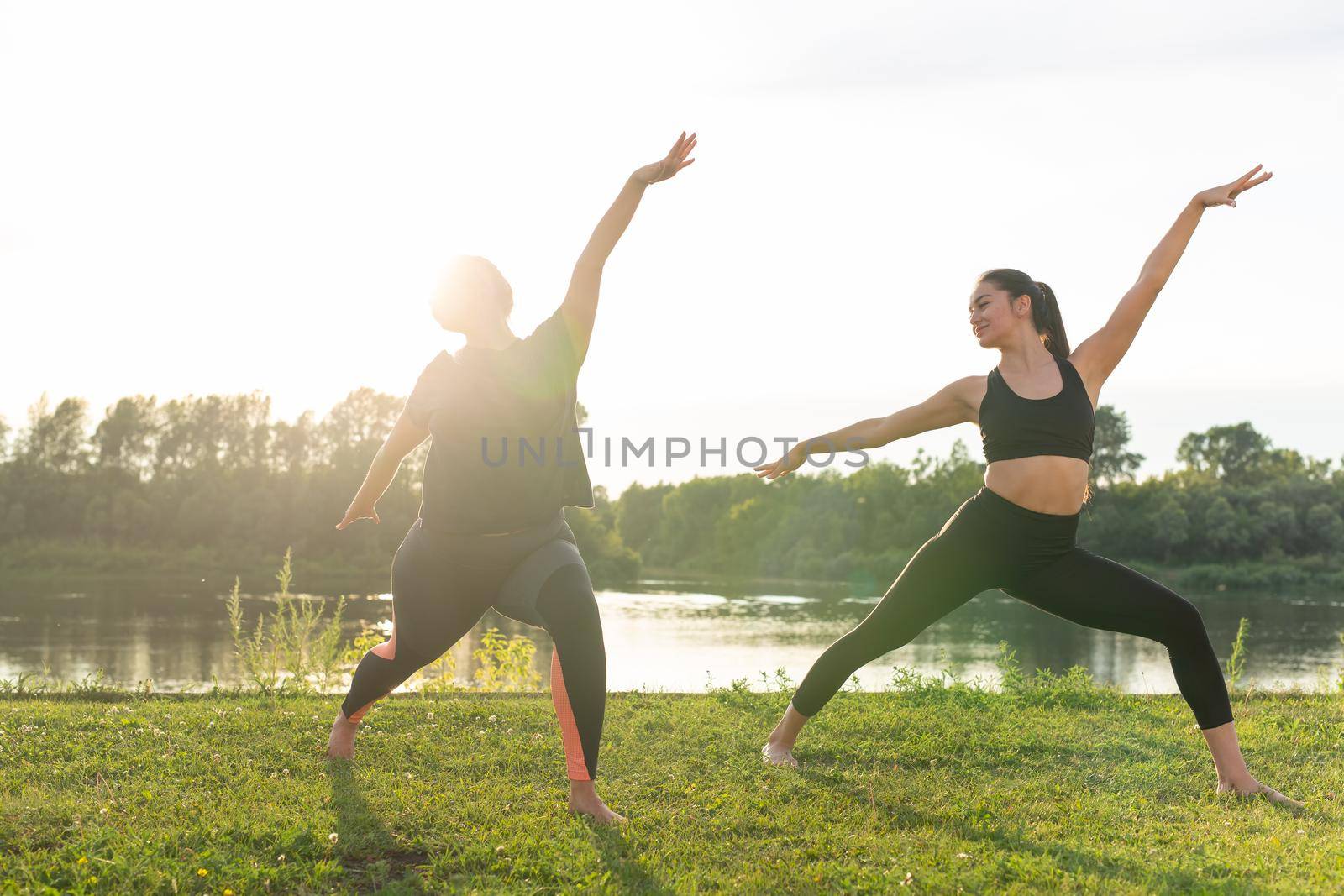 Harmony and healthy lifestyle concept - Young slim women in sportswear practicing yoga outdoors