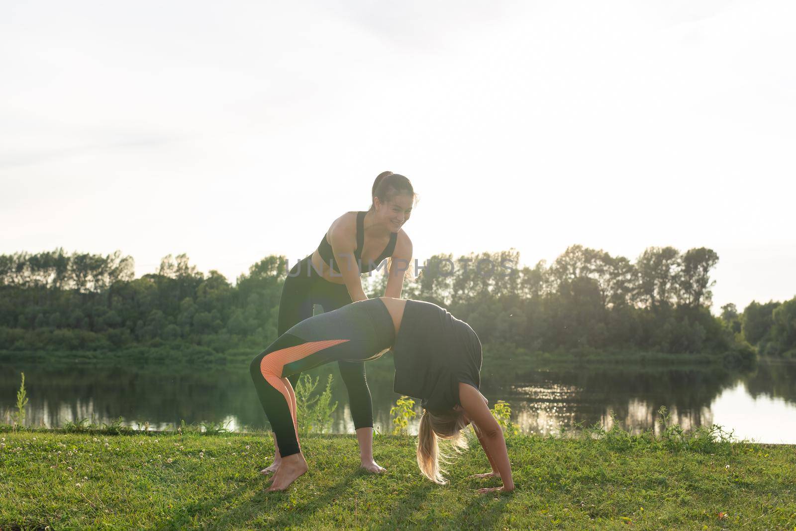 Harmony and healthy lifestyle concept - Young slim women in sportswear practicing yoga outdoors