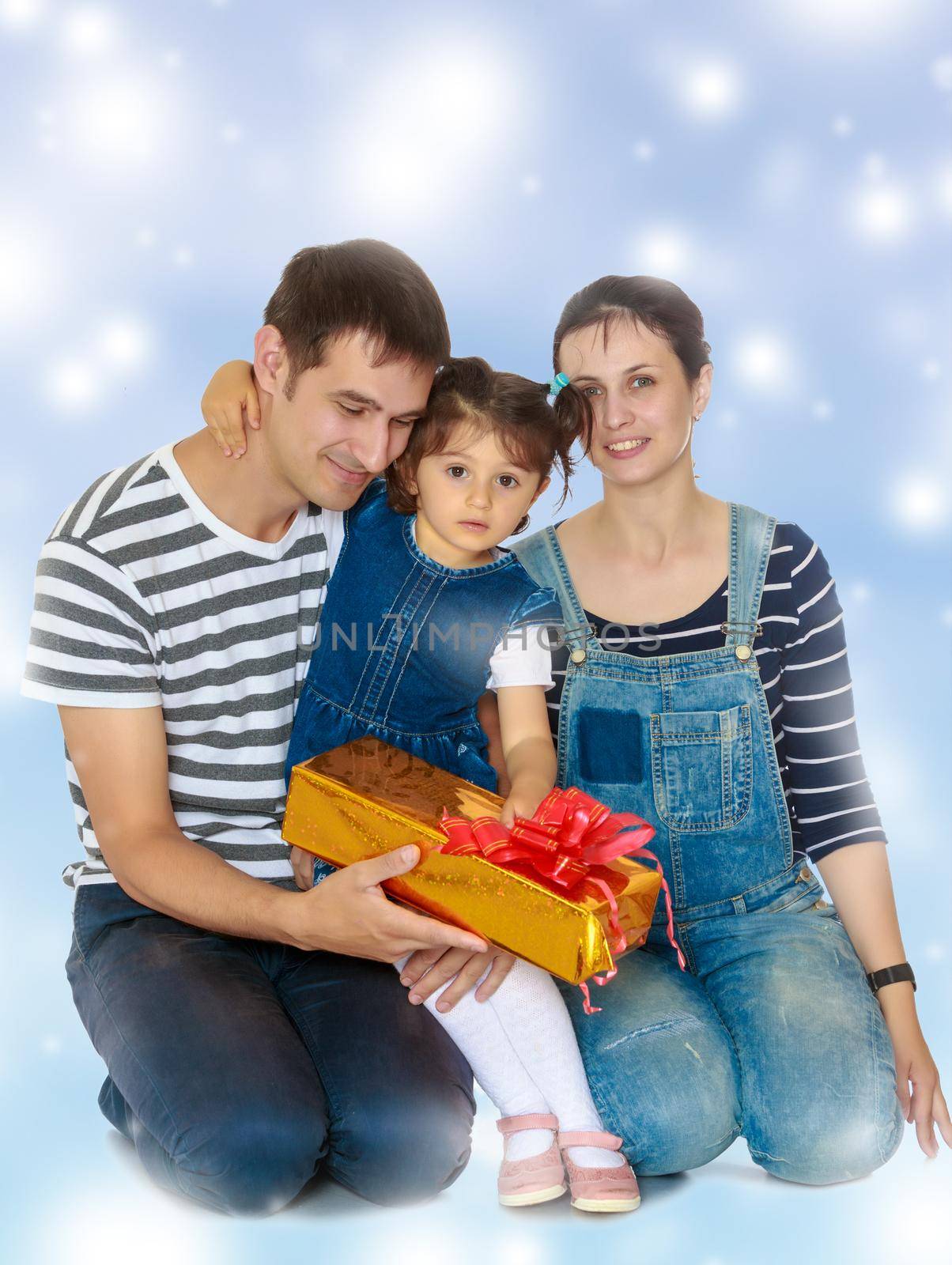 Happy young family with little daughter cuddling together in celebration of Christmas.Blue Christmas festive background with white snowflakes.