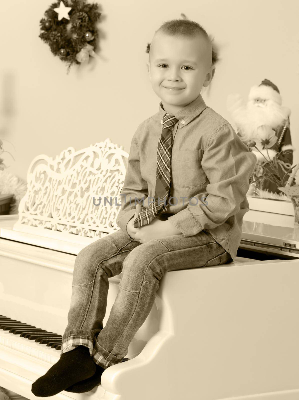 Elegant little boy in shirt and tie sitting on a white piano.In the Christmas night.Black-and-white photos , retro style.