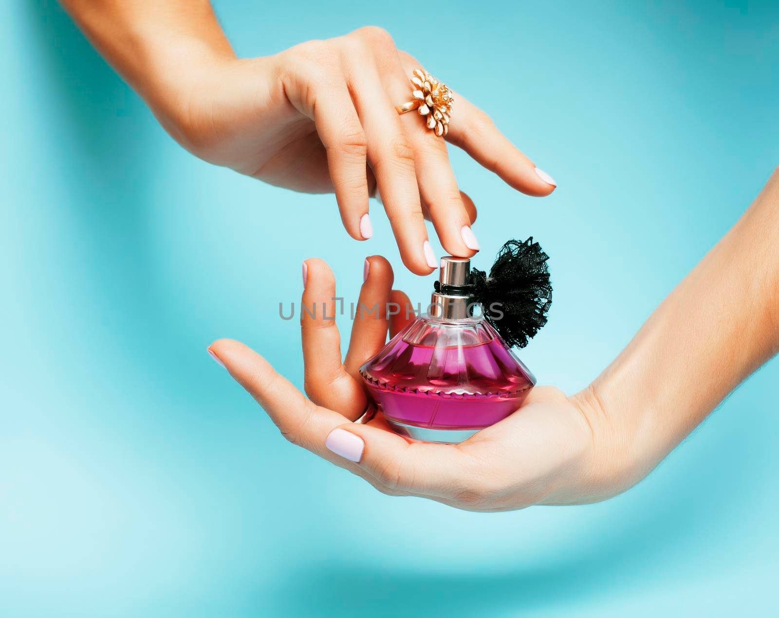 woman hands holding bottle of perfume pink manicure and jewelry on blue background, luxury concept close up