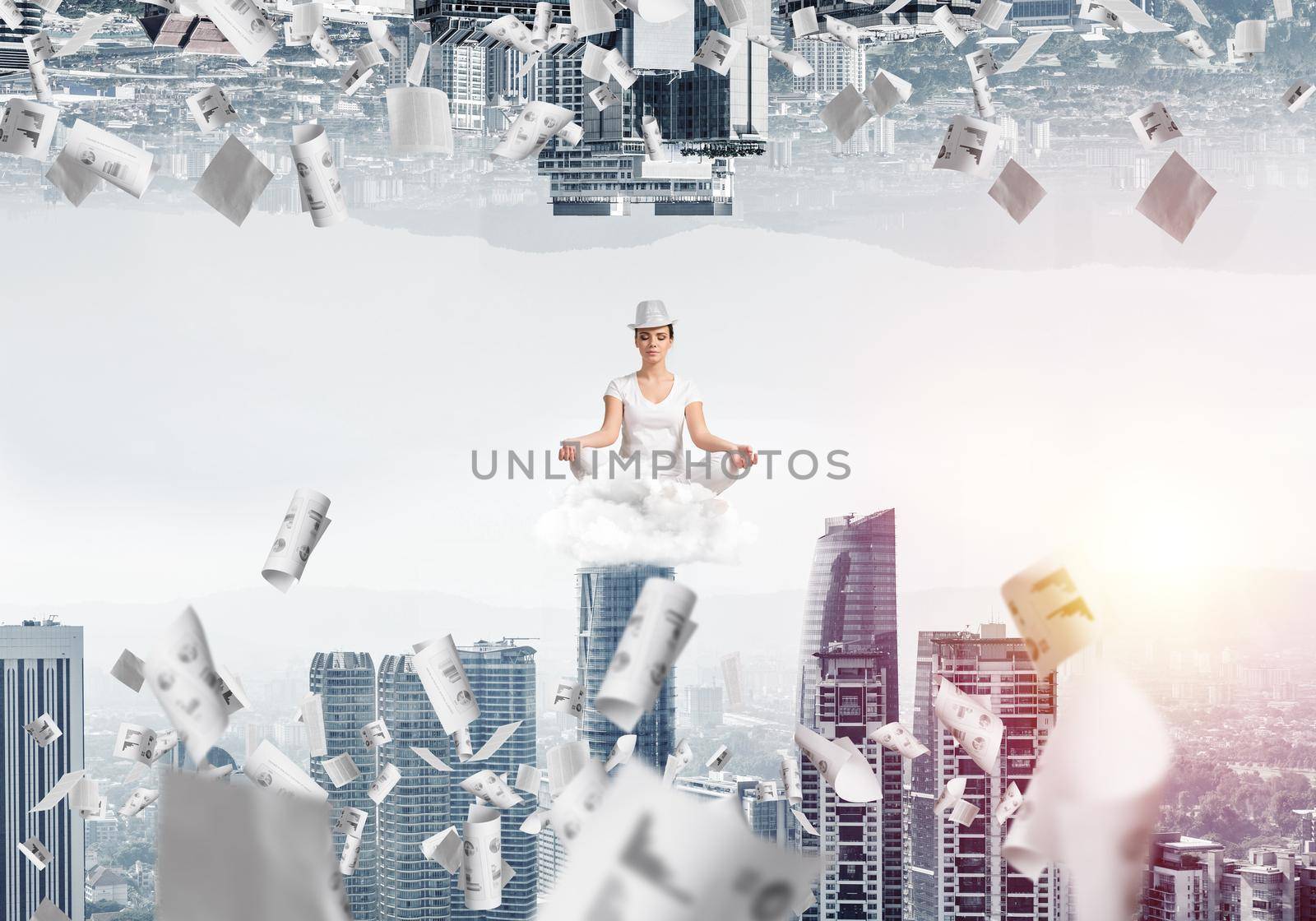 Young woman keeping eyes closed and looking concentrated while meditating on cloud among flying papers and between two urban worlds.