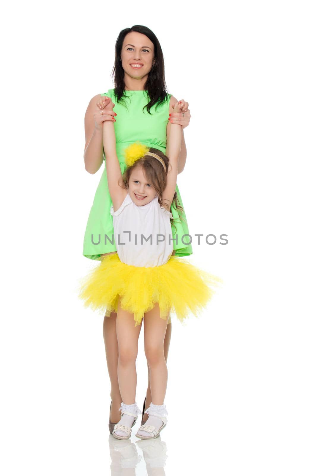 Beautiful young mother in a short green dress and her little beloved daughter in a yellow skirt.Fun mother throws daughter on hands.Isolated on white background.