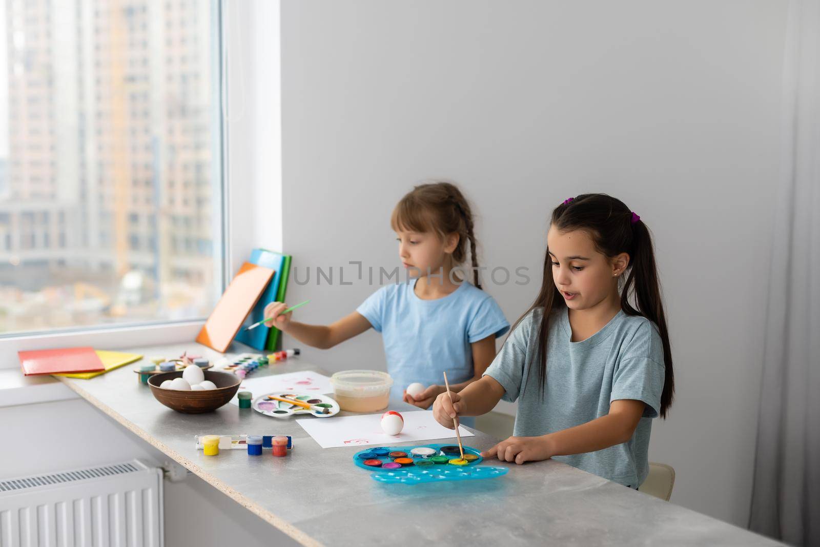 two little girls at the table with paints for drawing