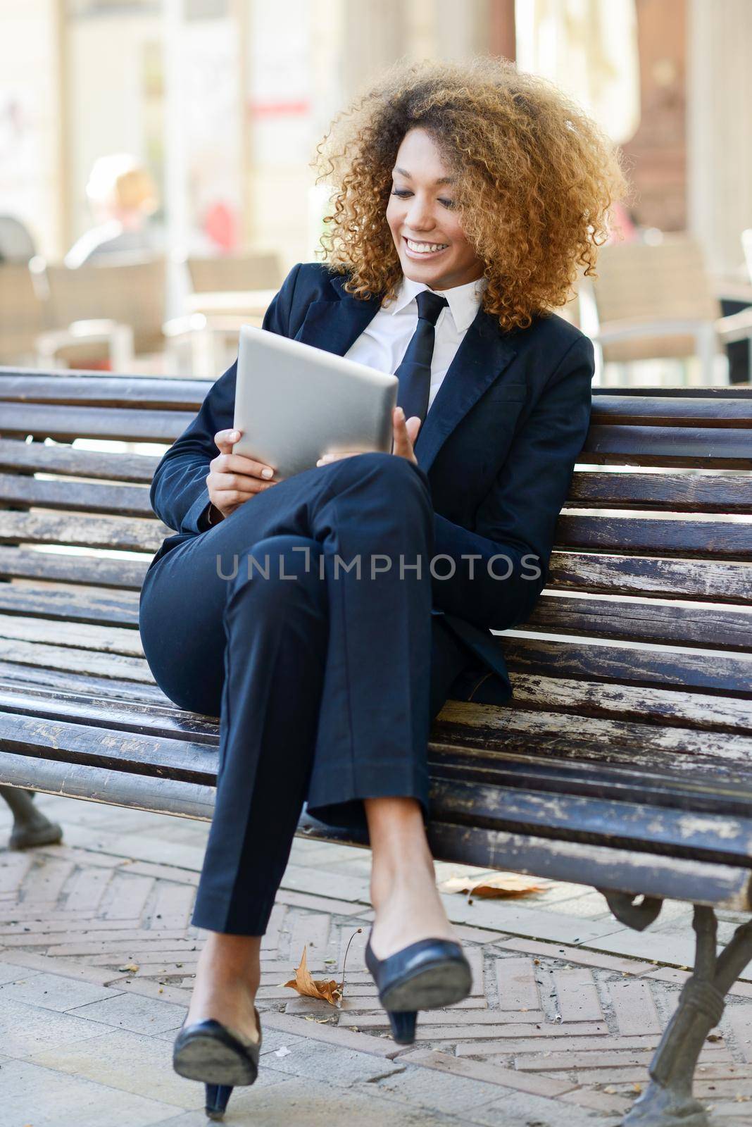 Beautiful black woman smiling and using tablet computer in urban background Businesswoman wearing suit with trousers and tie.